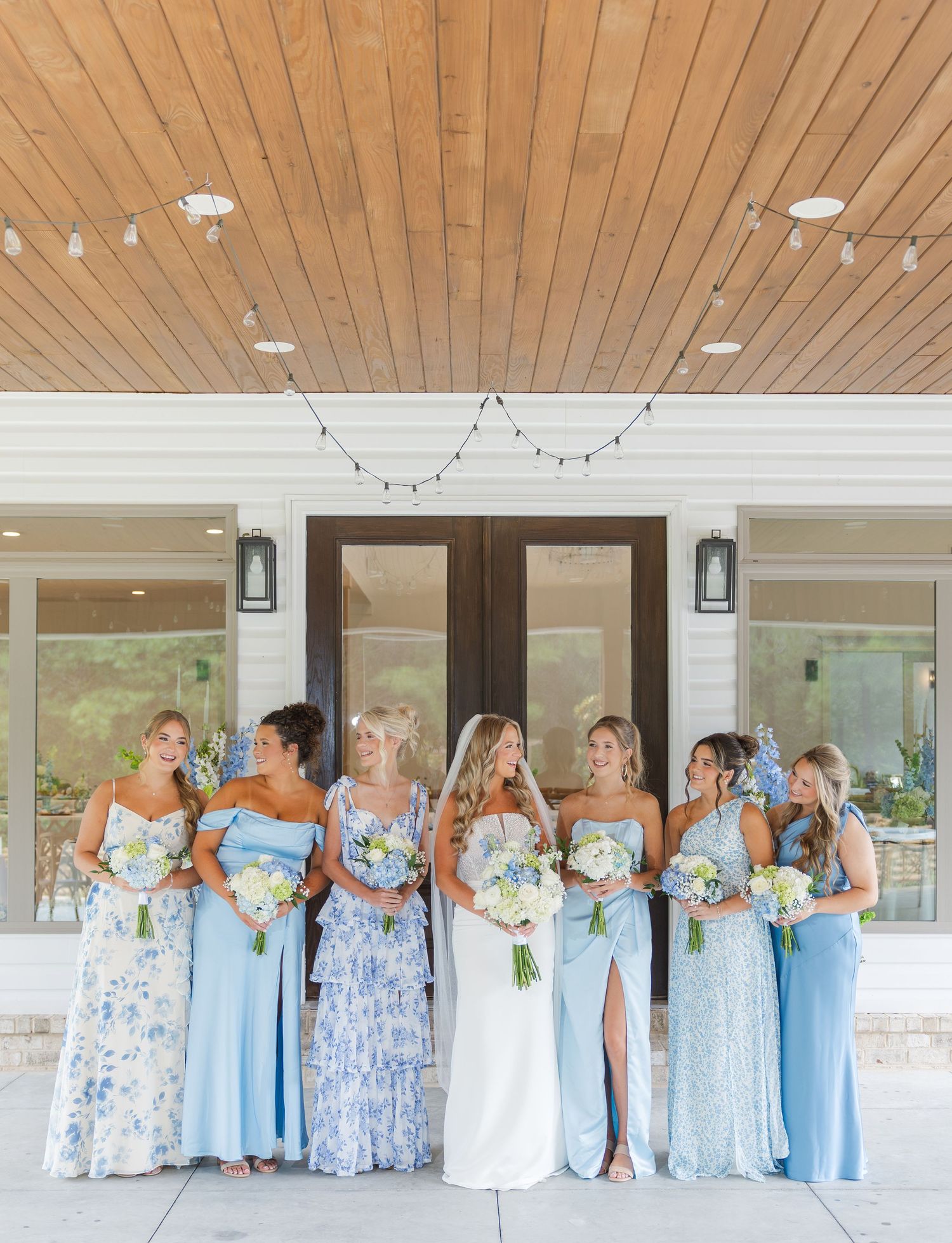 Bride with bridesmaids in mix of light blue and floral dresses holding white bouquets.