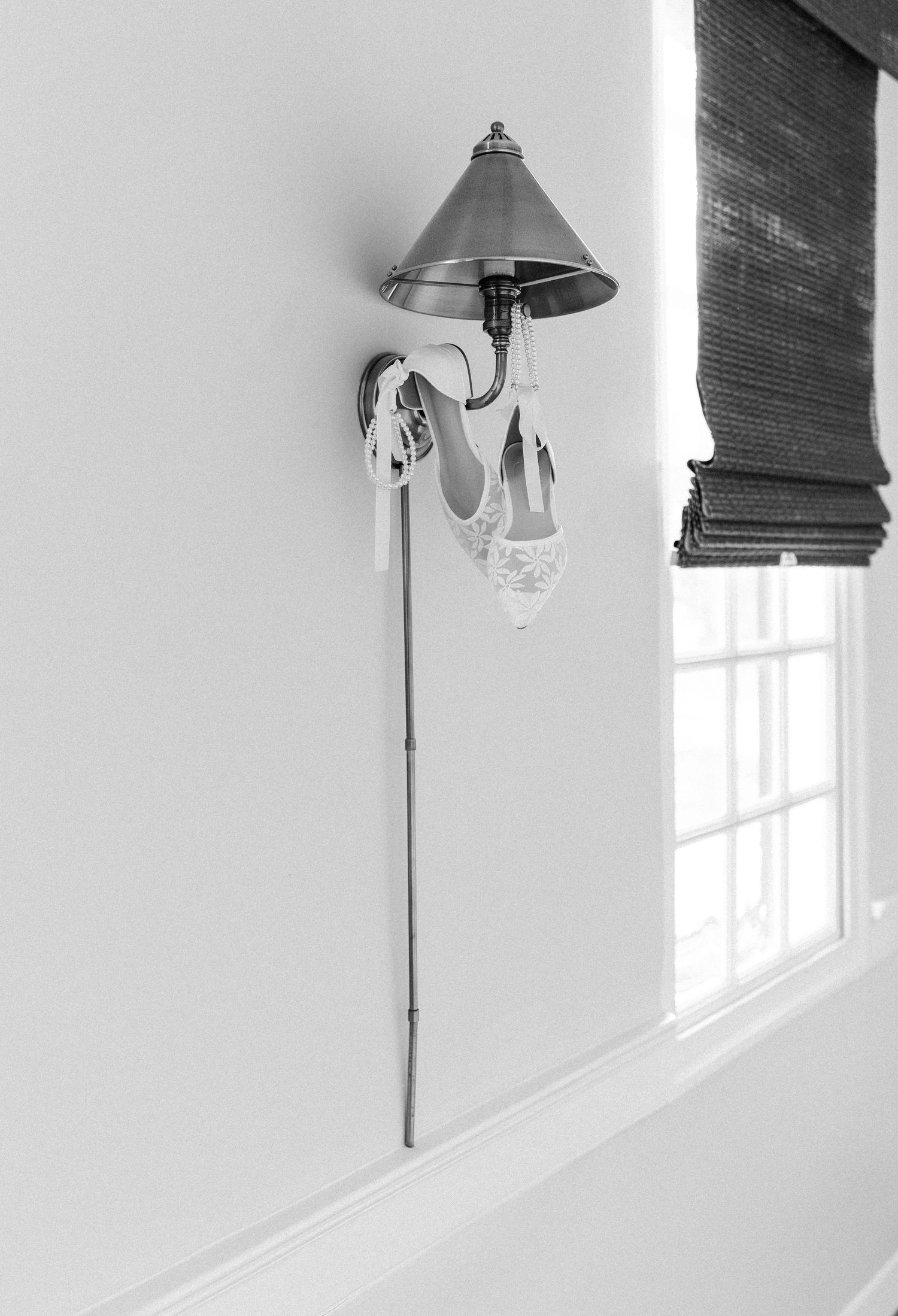 White lace bridal heels hanging on decorative wall sconce in black and white photo.