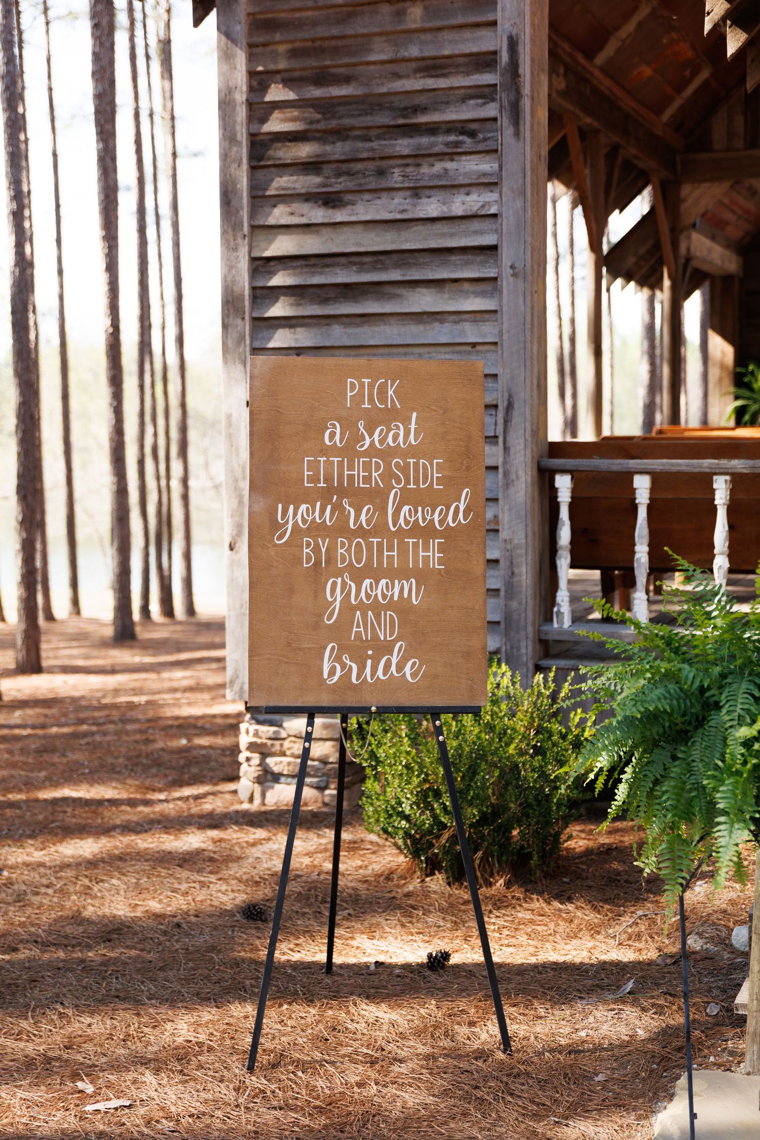 Rustic wedding seating sign on easel reading pick a seat either side you're loved by both the groom and bride.