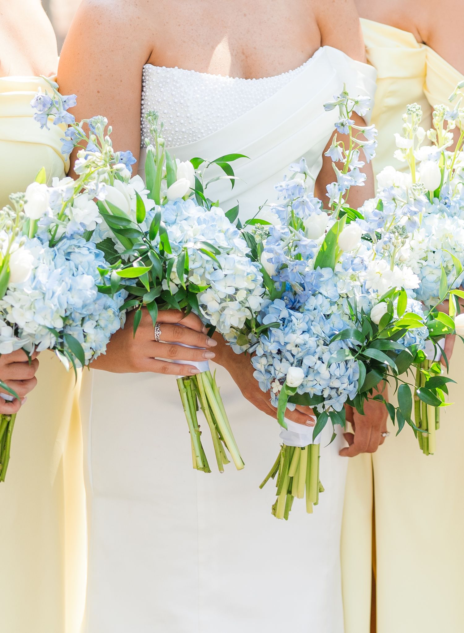 Close-up of blue hydrangea and white wedding bouquets held by bride and bridesmaids in yellow.