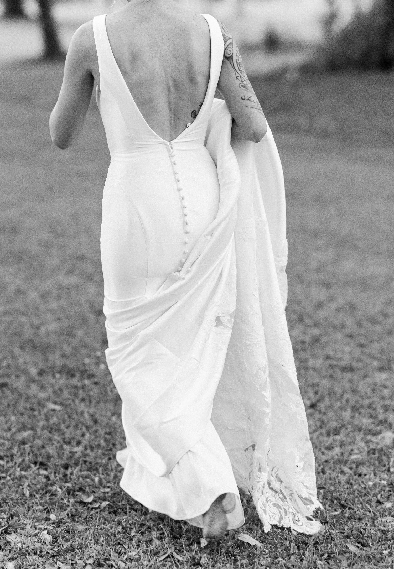 Black and white back view of bride in elegant white gown with low back and lace train on grass.