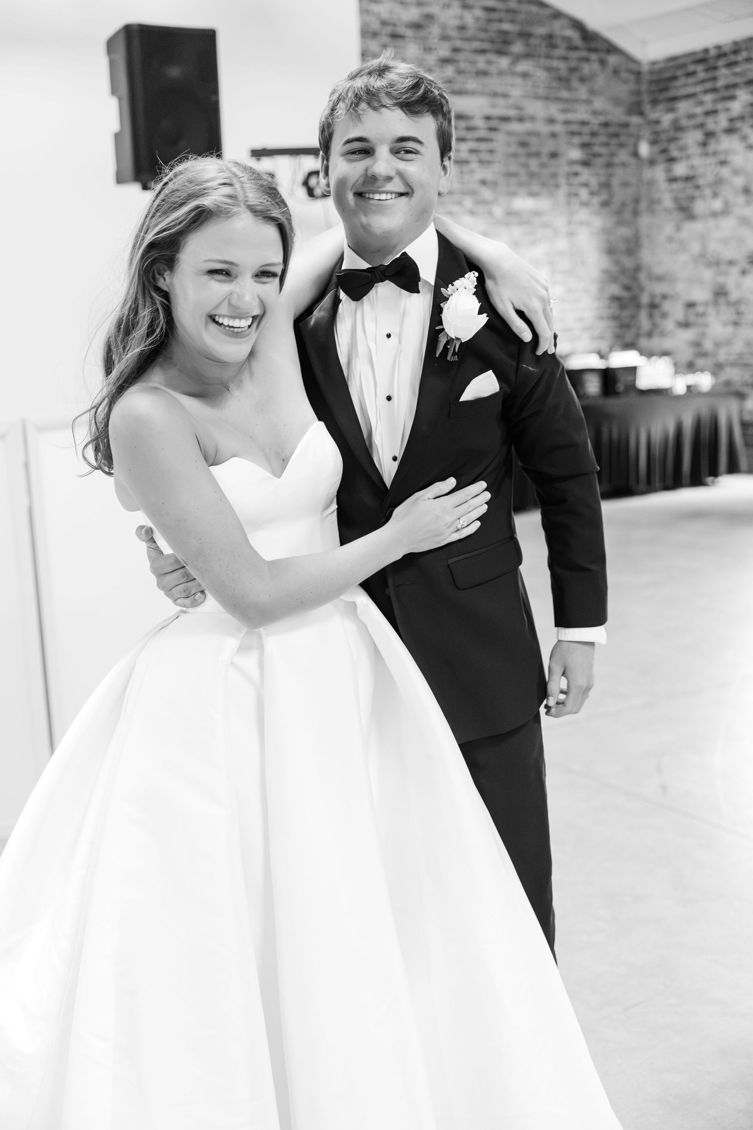Black and white portrait of laughing bride and groom embracing at wedding reception.
