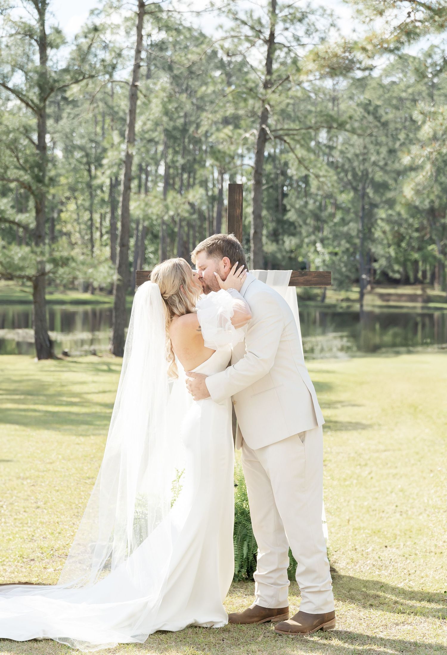 Newlyweds share intimate moment against backdrop of pine trees and lake during wedding.