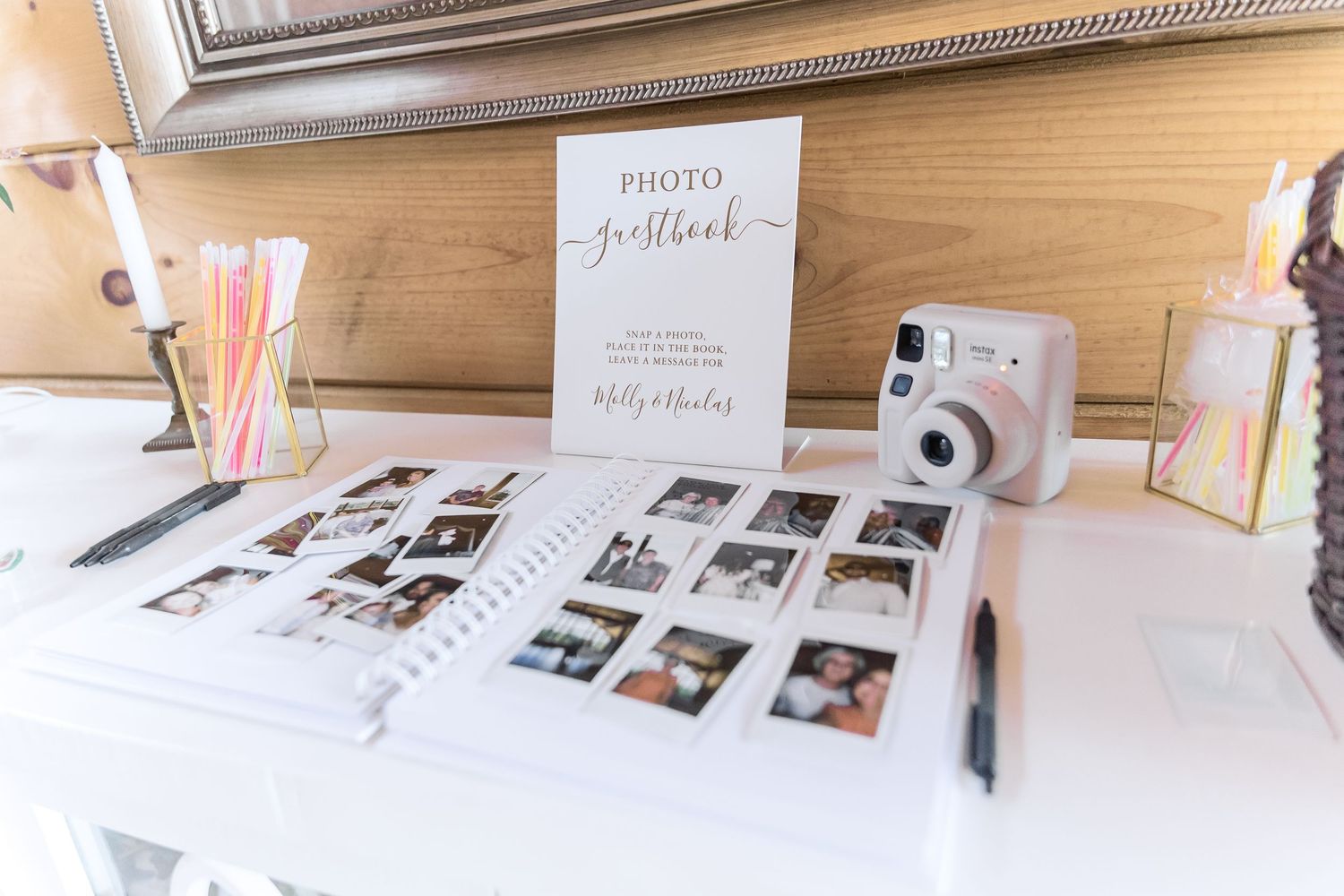 Wedding photo guestbook setup with instant camera and pink straws on display.