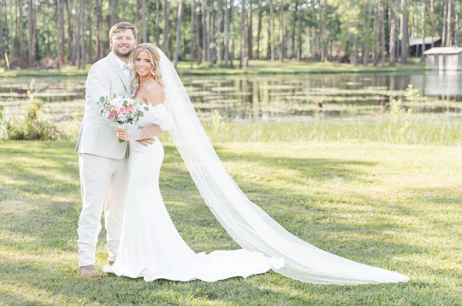 An ethereal wedding photo with a sweeping cathedral veil against a lakeside setting.