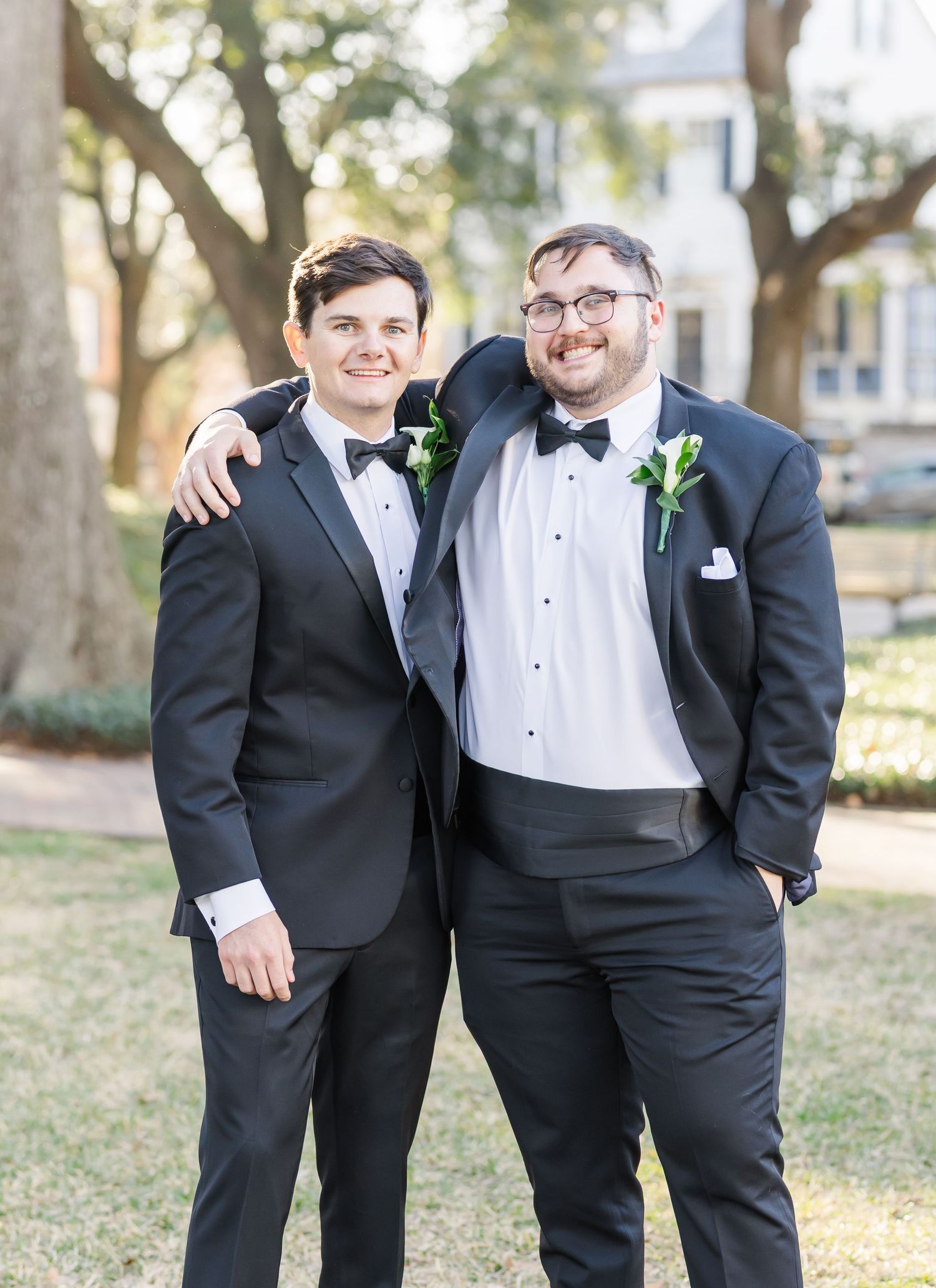 Groomsmen in classic black tuxedos share laughs during outdoor wedding photo session.