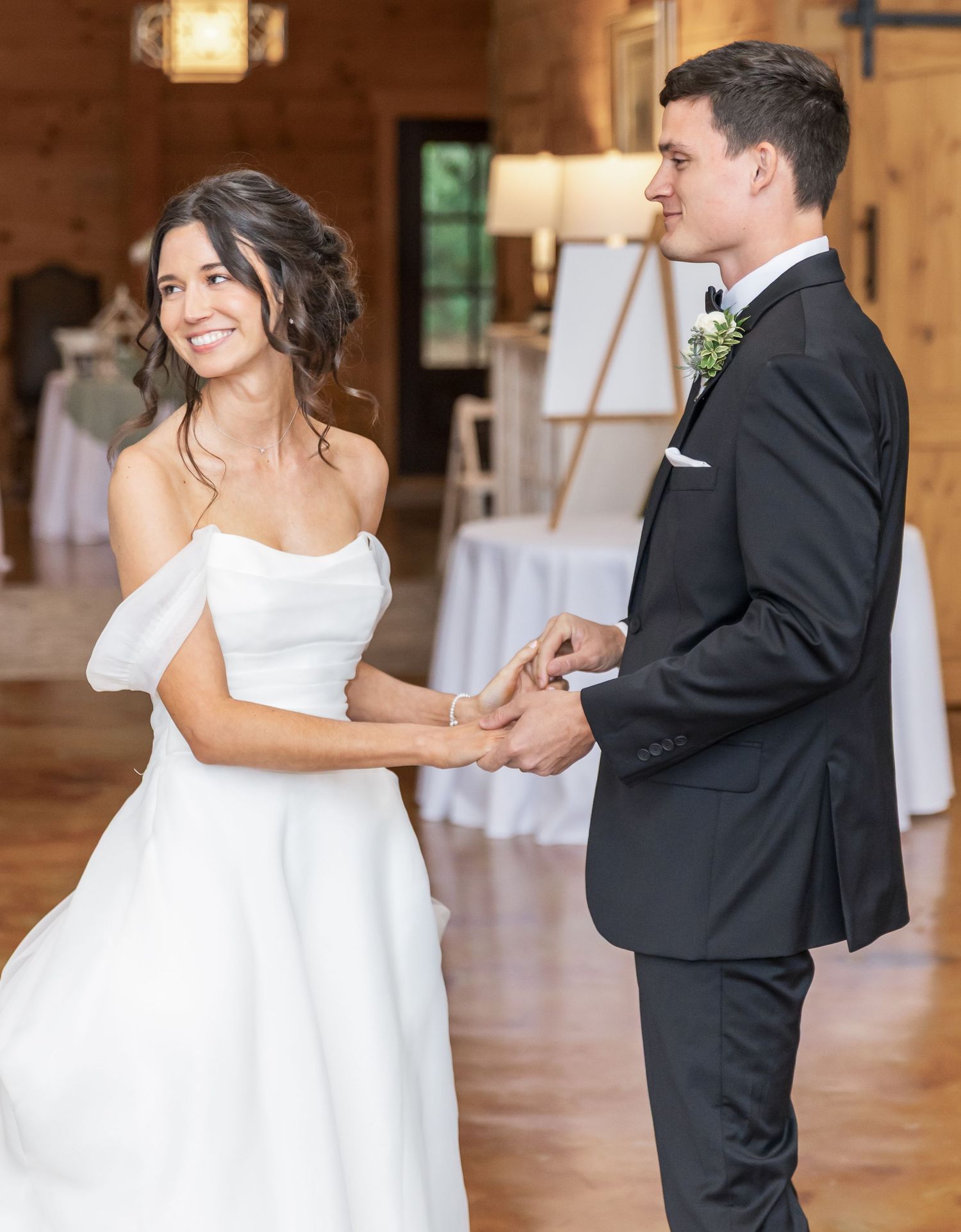 A couple in formal wedding attire dancing together in an elegant wooden barn venue.