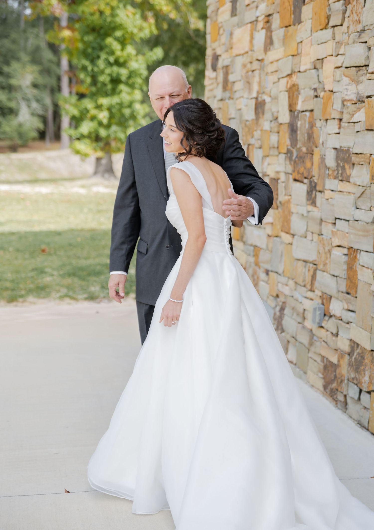 A tender wedding moment captured against a rustic stone wall backdrop with the bride in a flowing white gown.