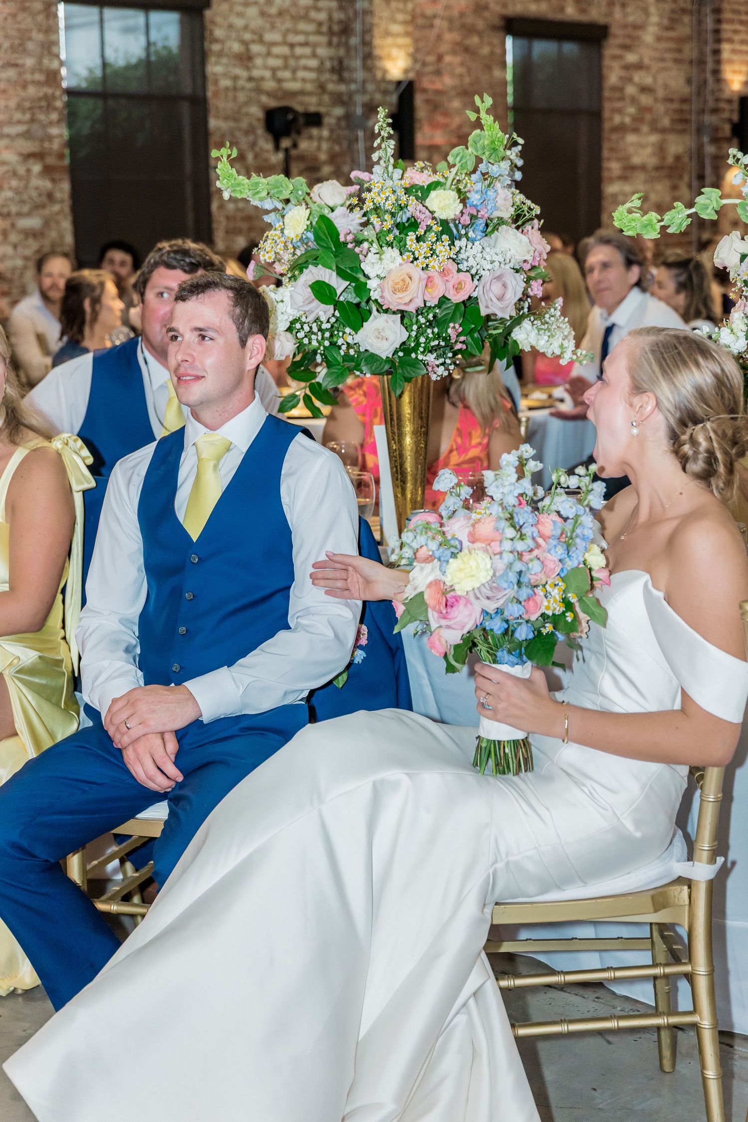 Wedding celebration in an industrial brick venue with elegant gold chairs and floral decorations.