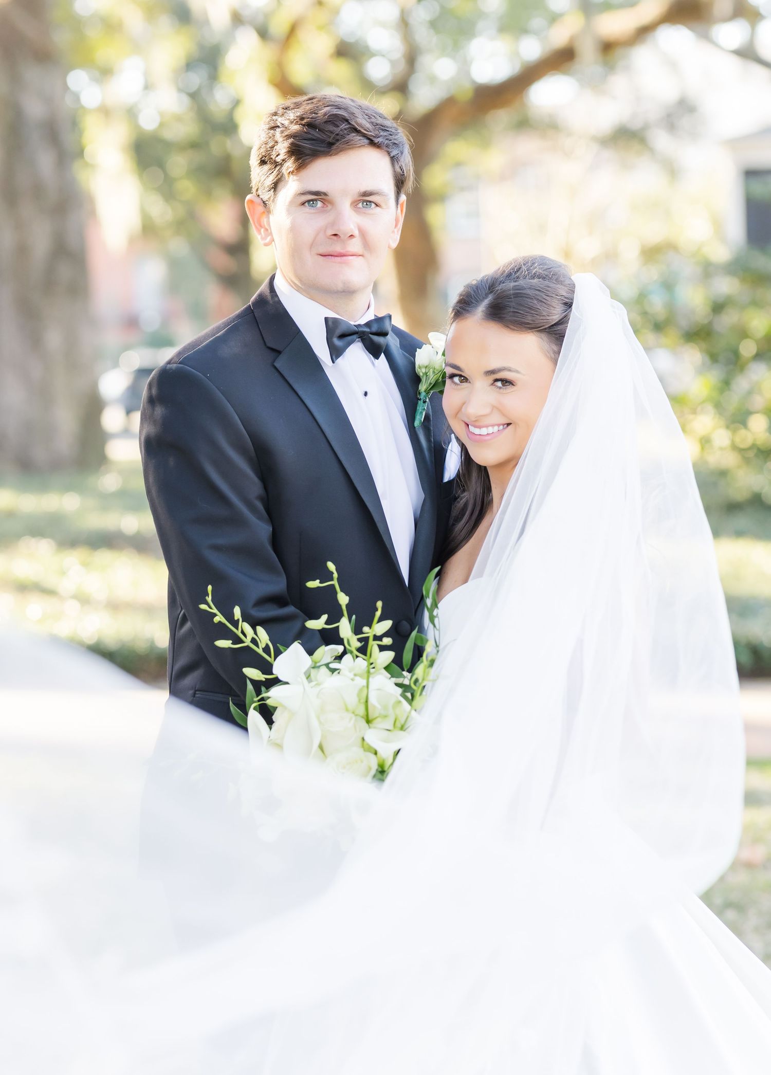 Romantic bride and groom portraits with flowing veil and white bouquet in natural outdoor setting.