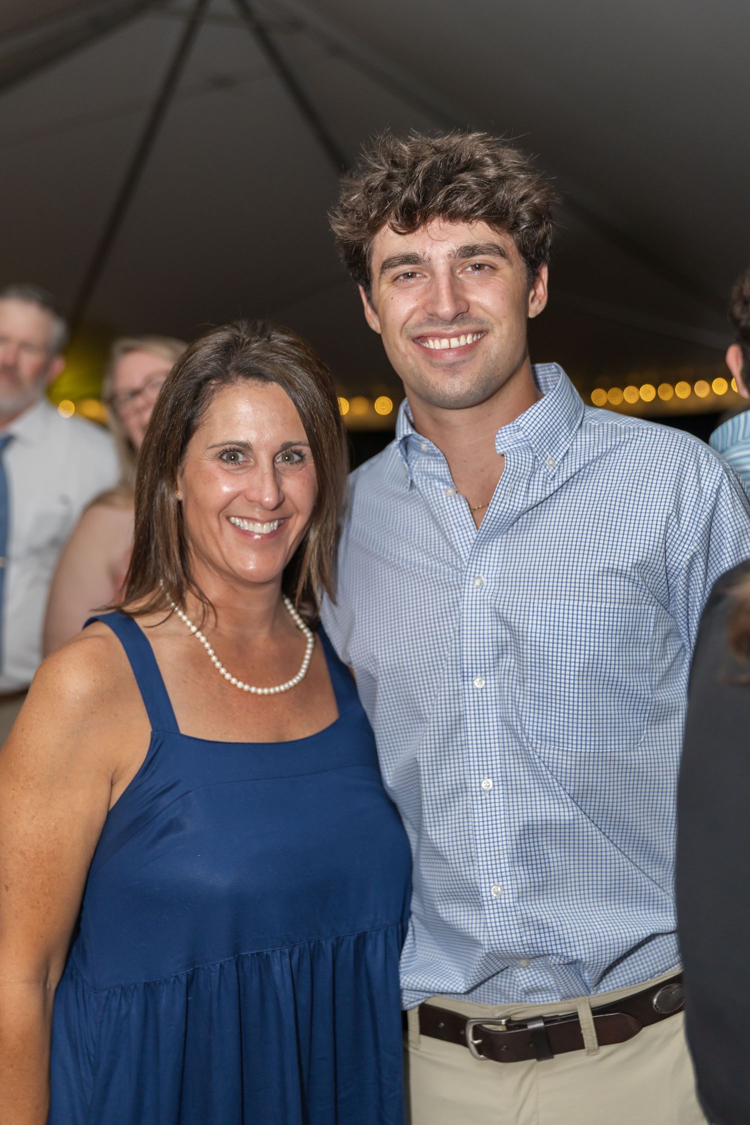 Couples in blue and white attire pose together at an evening celebration under string lights.