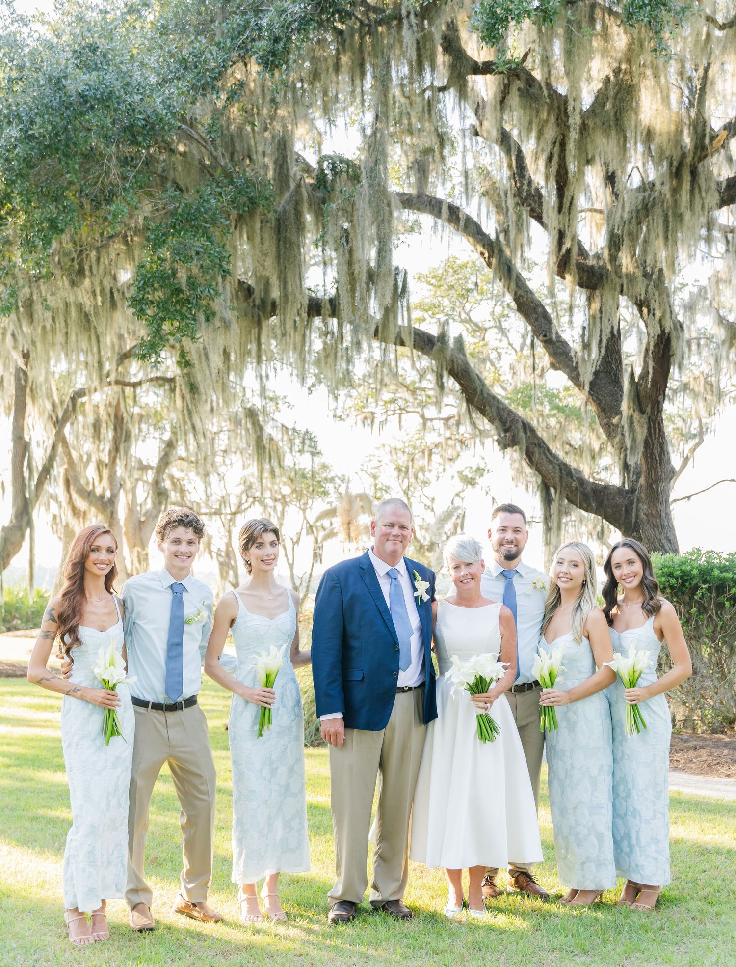 Wedding party poses together under Spanish moss draped trees in a scenic outdoor garden setting.