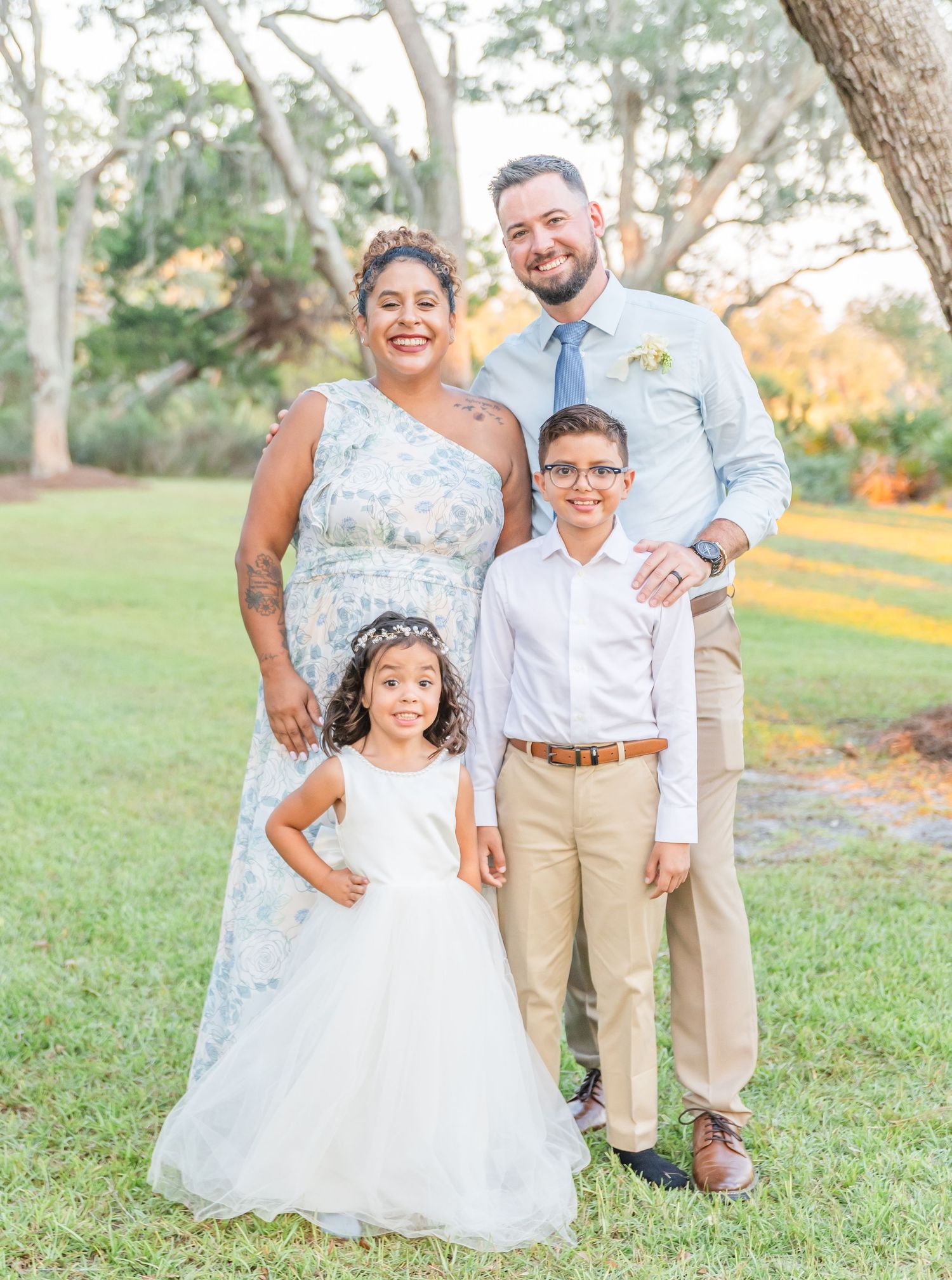 Family portraits taken outdoors in a grassy field wearing coordinated beige and white outfits at sunset.