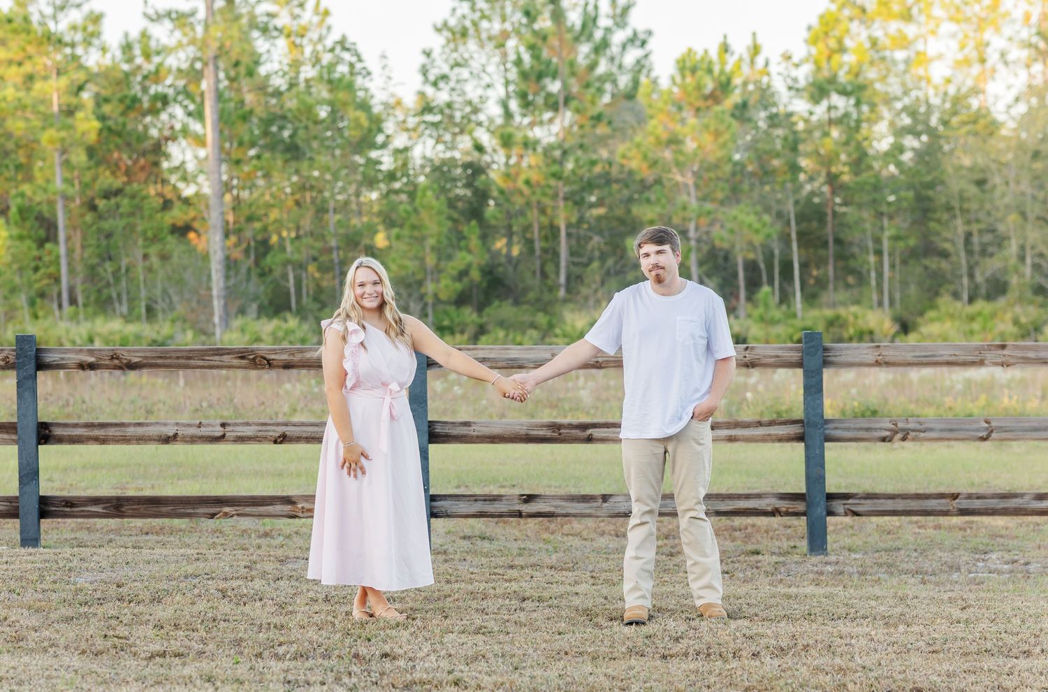 A couple in white outfits walks together across a rustic outdoor setting during a photo session.