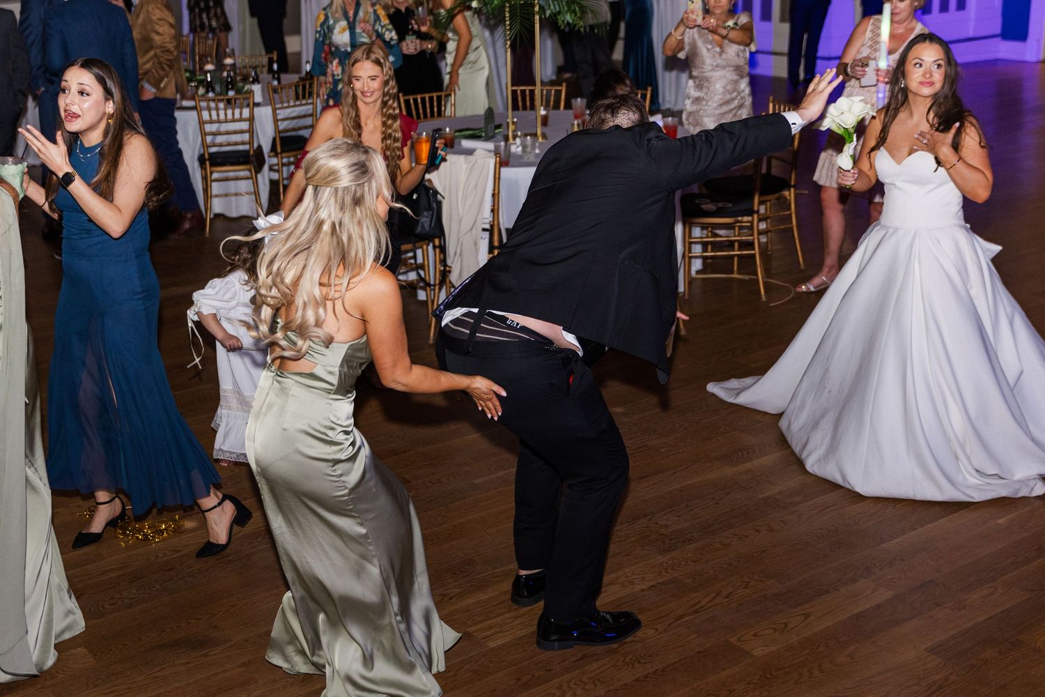 Wedding guests dance with bride in white gown at lively reception party.