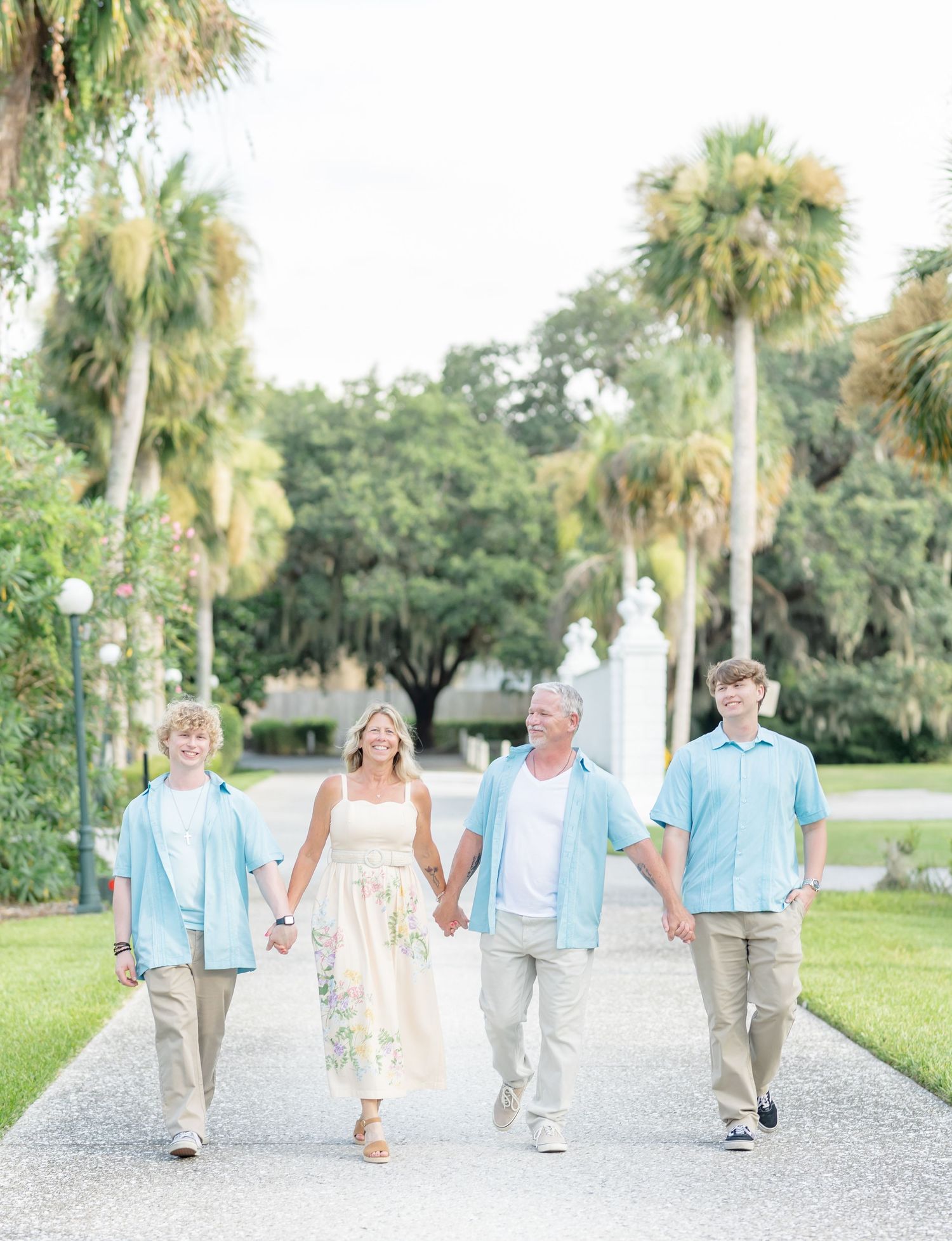 A cheerful group walks along a white gravel path lined with palm trees in matching light blue and khaki outfits.