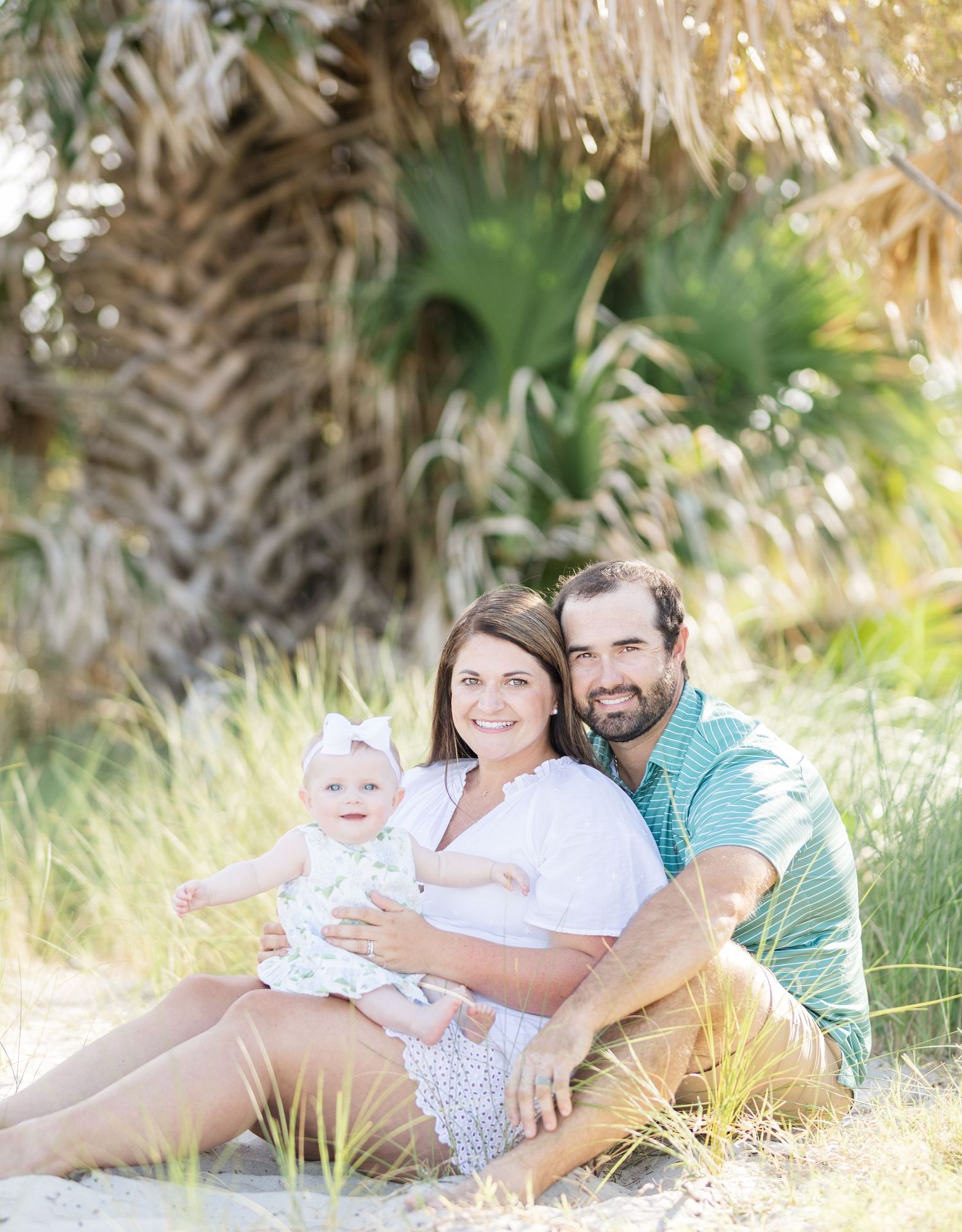 A family relaxes together on sand dunes with palm trees creating a dreamy beach atmosphere during sunset.