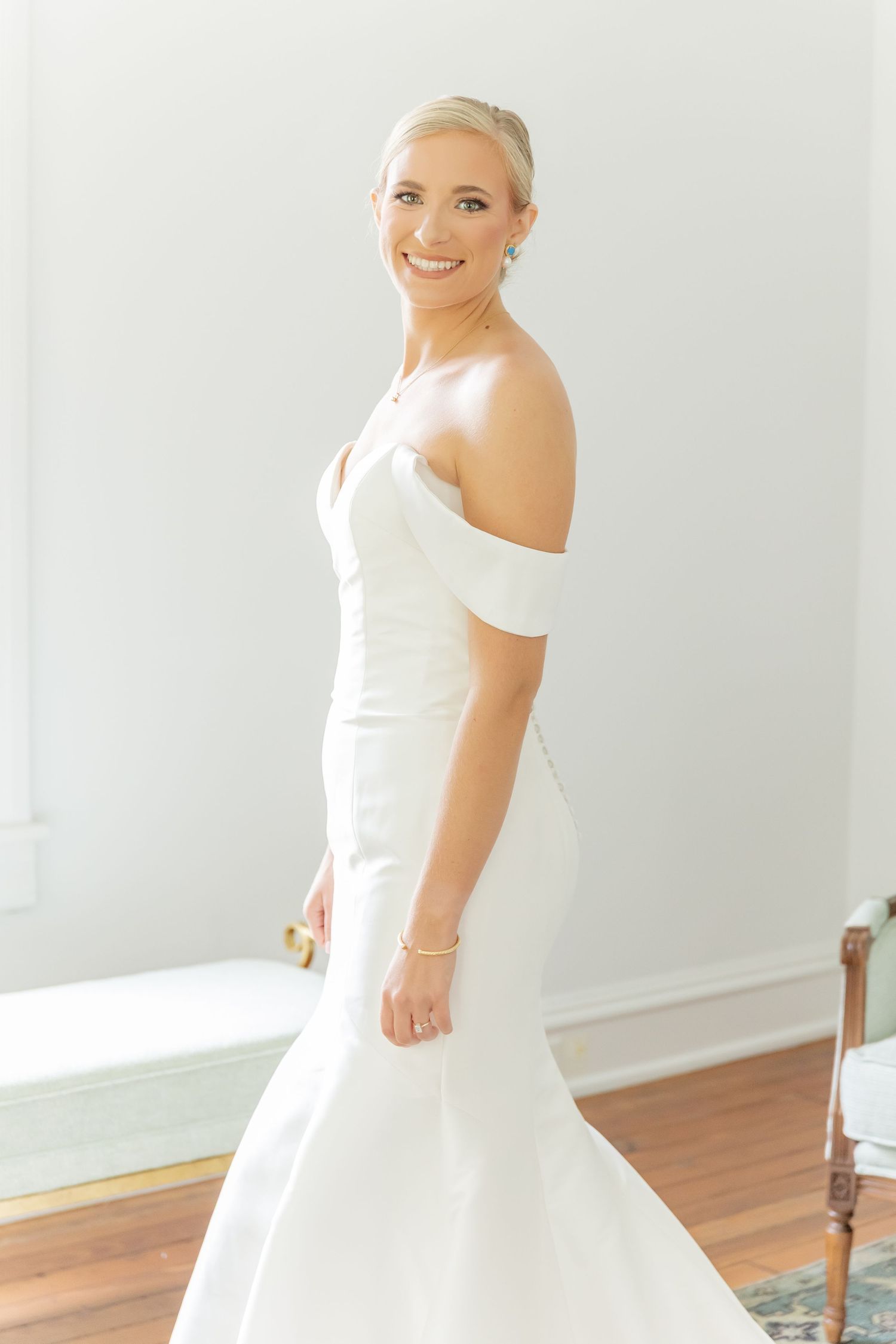 An elegant off-shoulder mermaid wedding gown displayed in a bright interior setting.