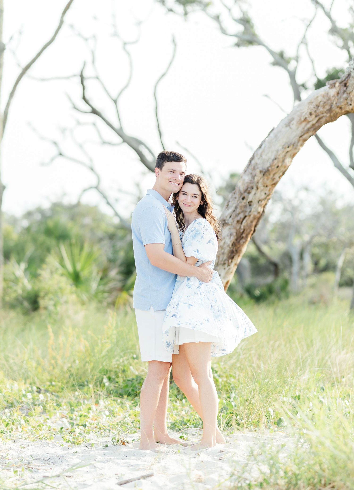 Couple sharing sweet moments near trees in a grassy outdoor area.