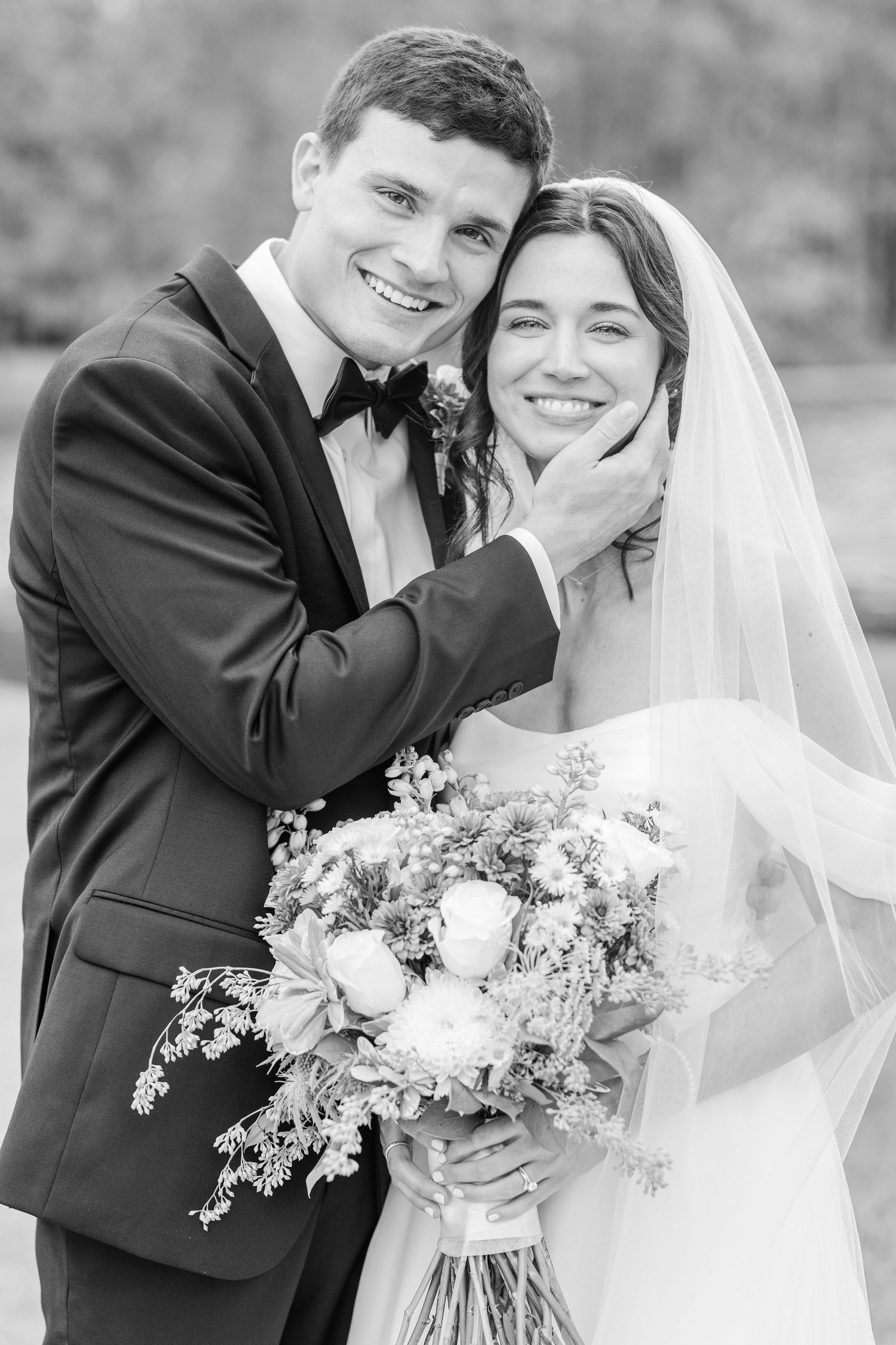 A black and white portrait of newlyweds sharing an intimate moment with a floral bouquet.