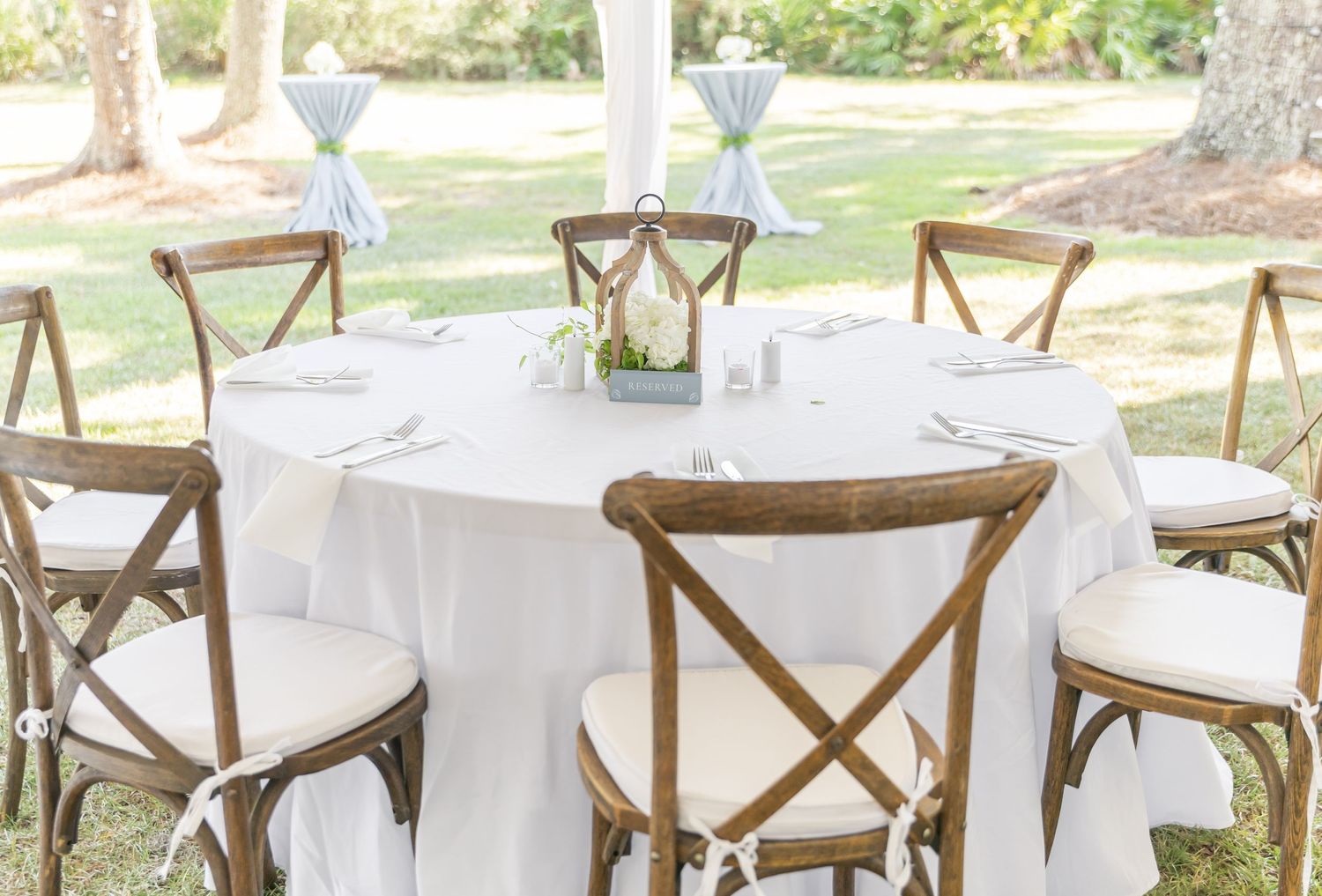 Elegant outdoor reception setup with cross-back chairs and round tables under a white tent.