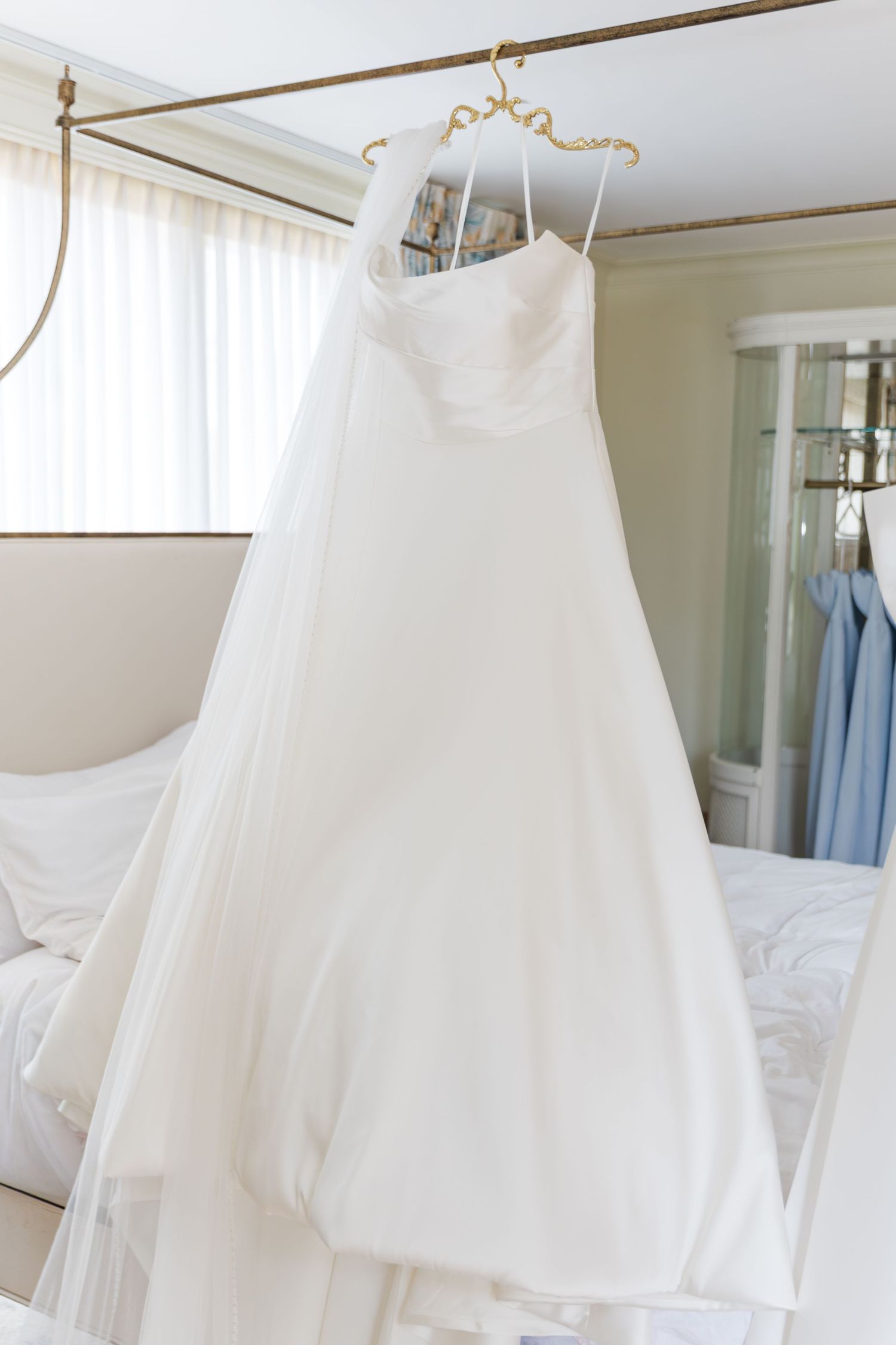 White strapless ball gown wedding dress hanging on a gold hanger in a bright bedroom.