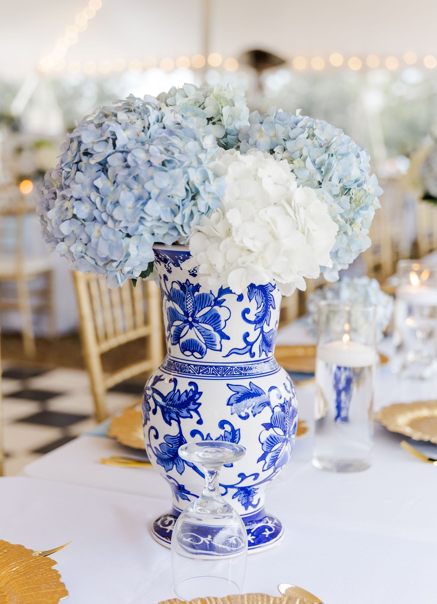 Tall blue and white chinoiserie vase centerpiece overflowing with blue and white hydrangeas at wedding reception.