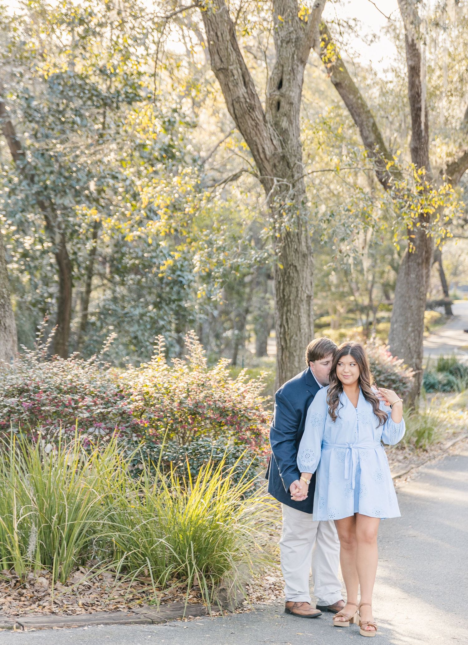 Romantic couple standing together on a scenic park pathway surrounded by trees.