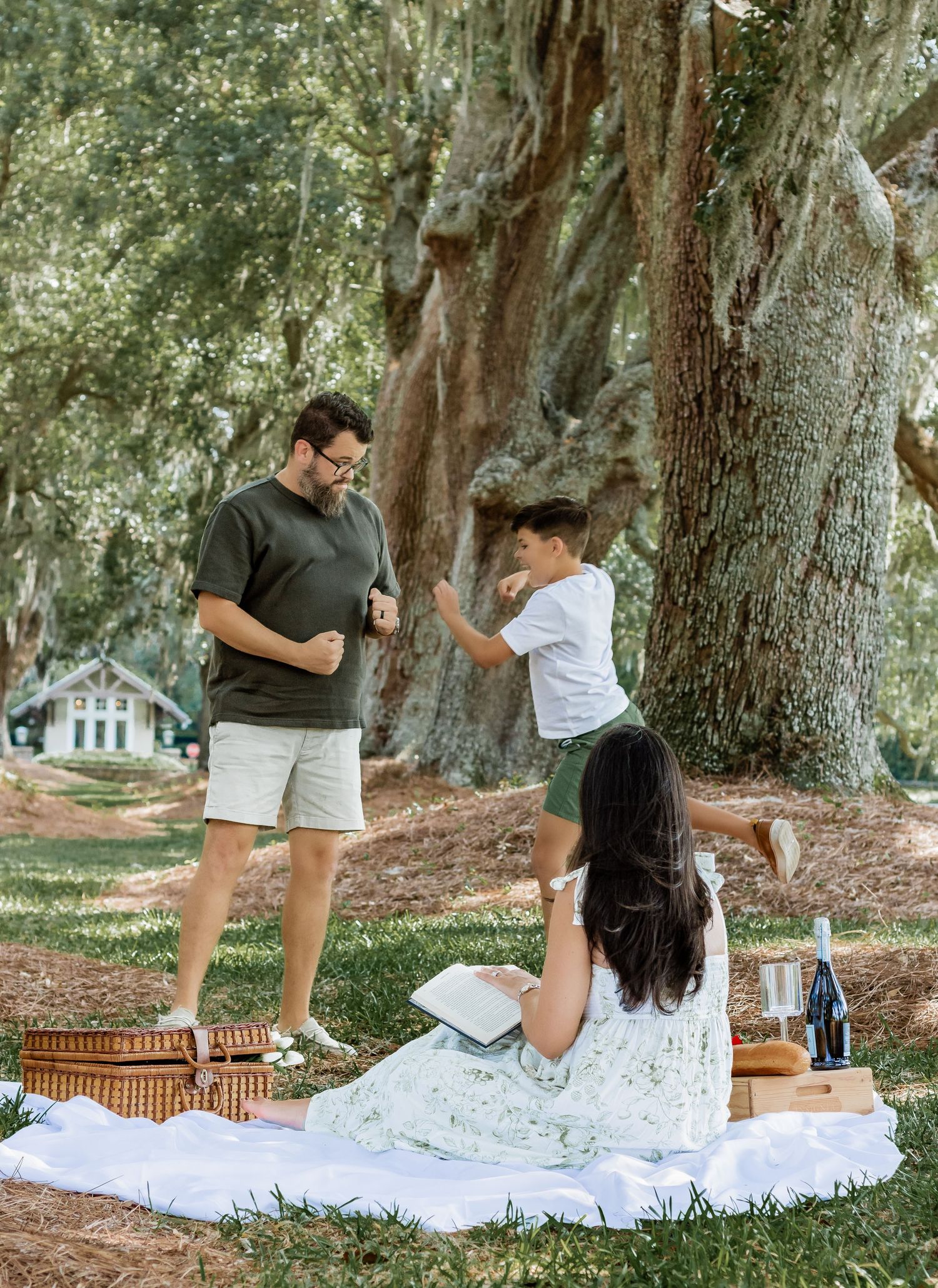 Family members having fun and dancing during their outdoor picnic beneath large trees.