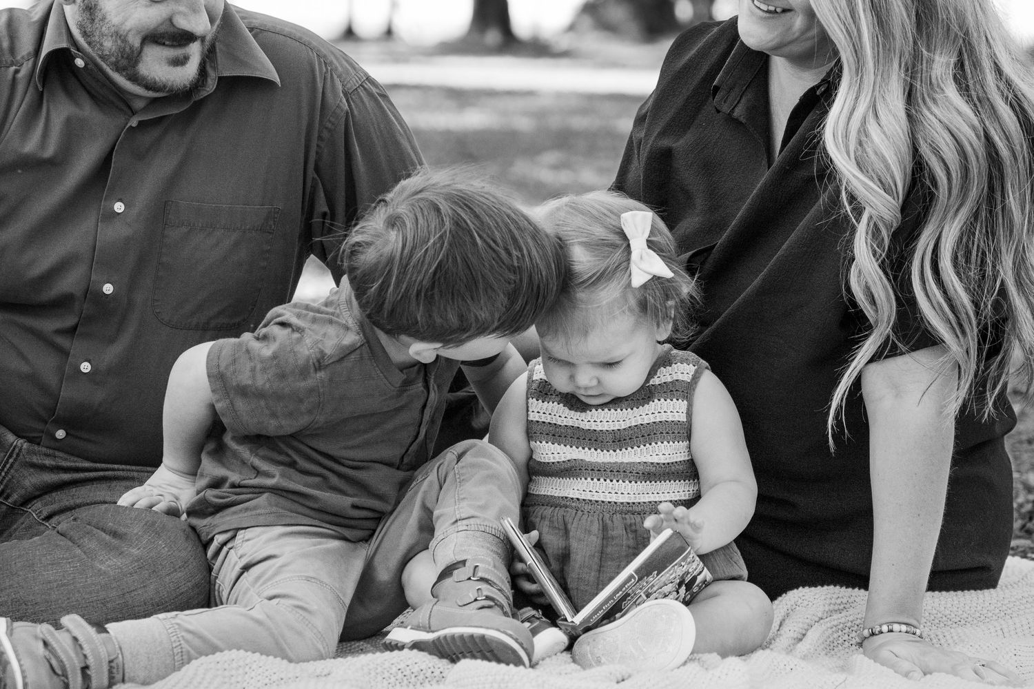 Black and white photo of a family sharing a heartwarming reading moment together on a couch.