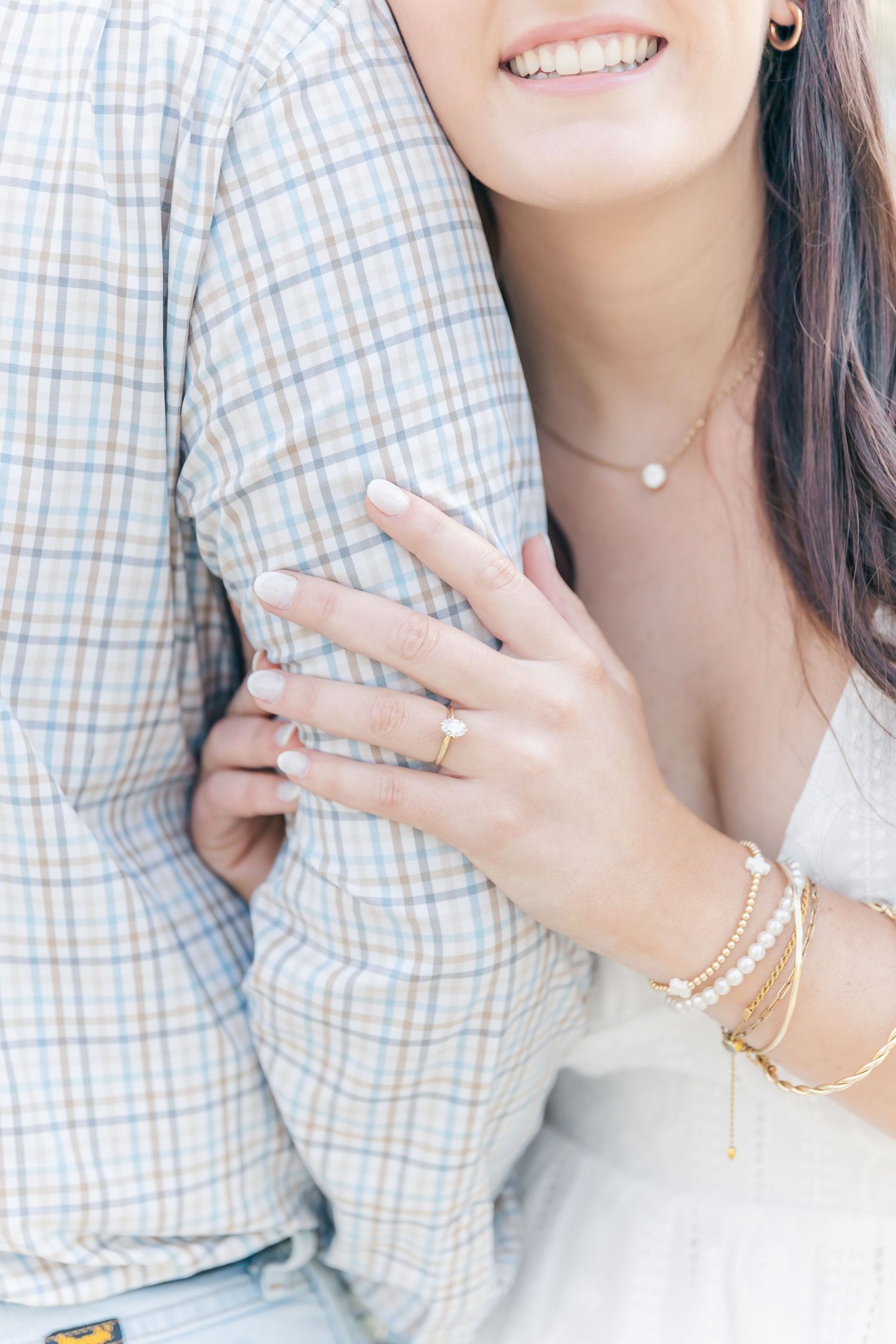 Close-up of an engagement ring and delicate jewelry against a plaid shirt.