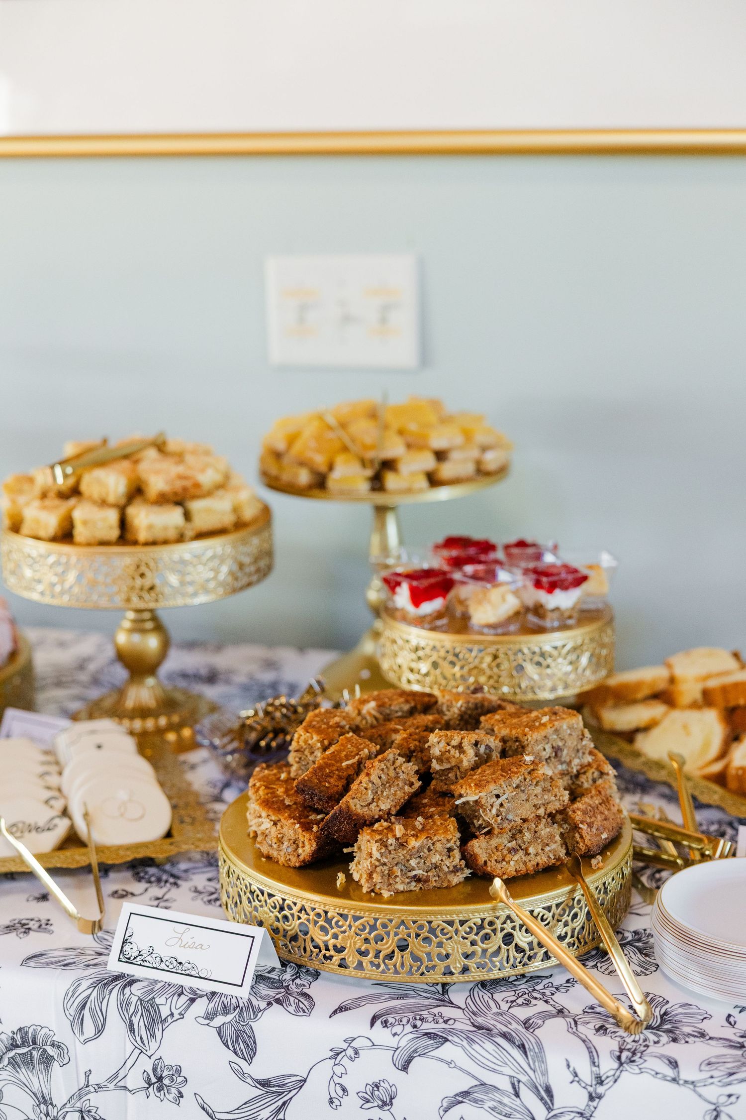 Elegant gold dessert stands display assorted pastries, brownies, and petit fours on a floral tablecloth at an upscale event.
