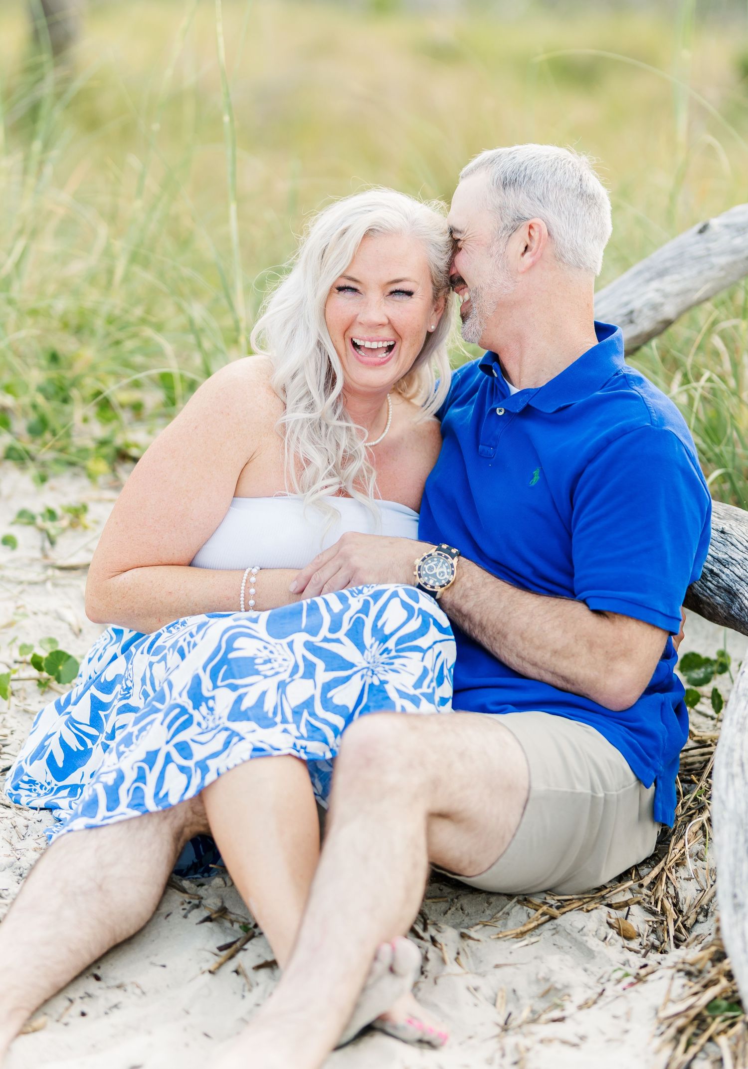 A couple shares a joyful moment together on a sandy beach, wearing coordinating blue and white outfits.