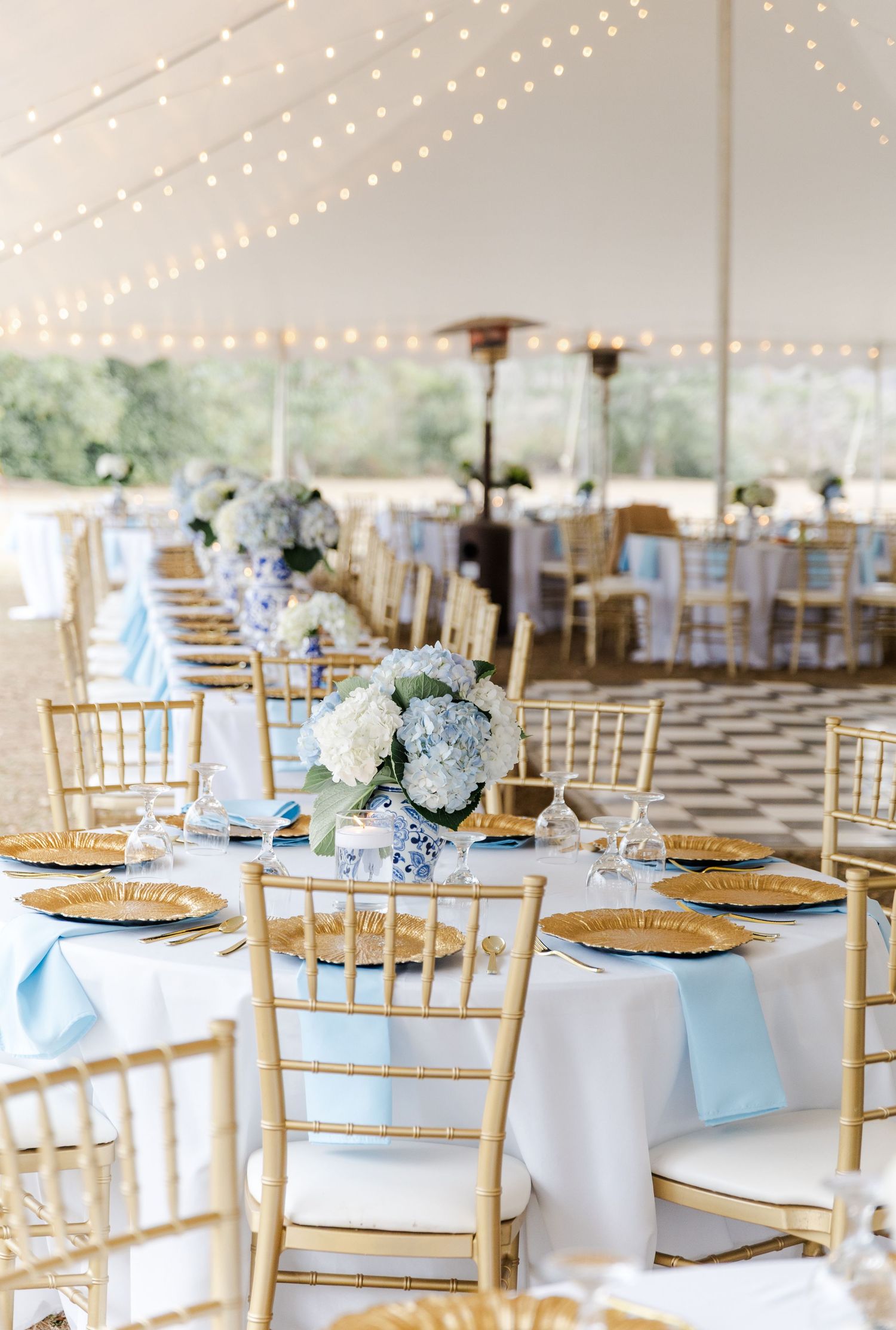 Elegant wedding reception under tent with gold chiavari chairs and blue hydrangea centerpieces.