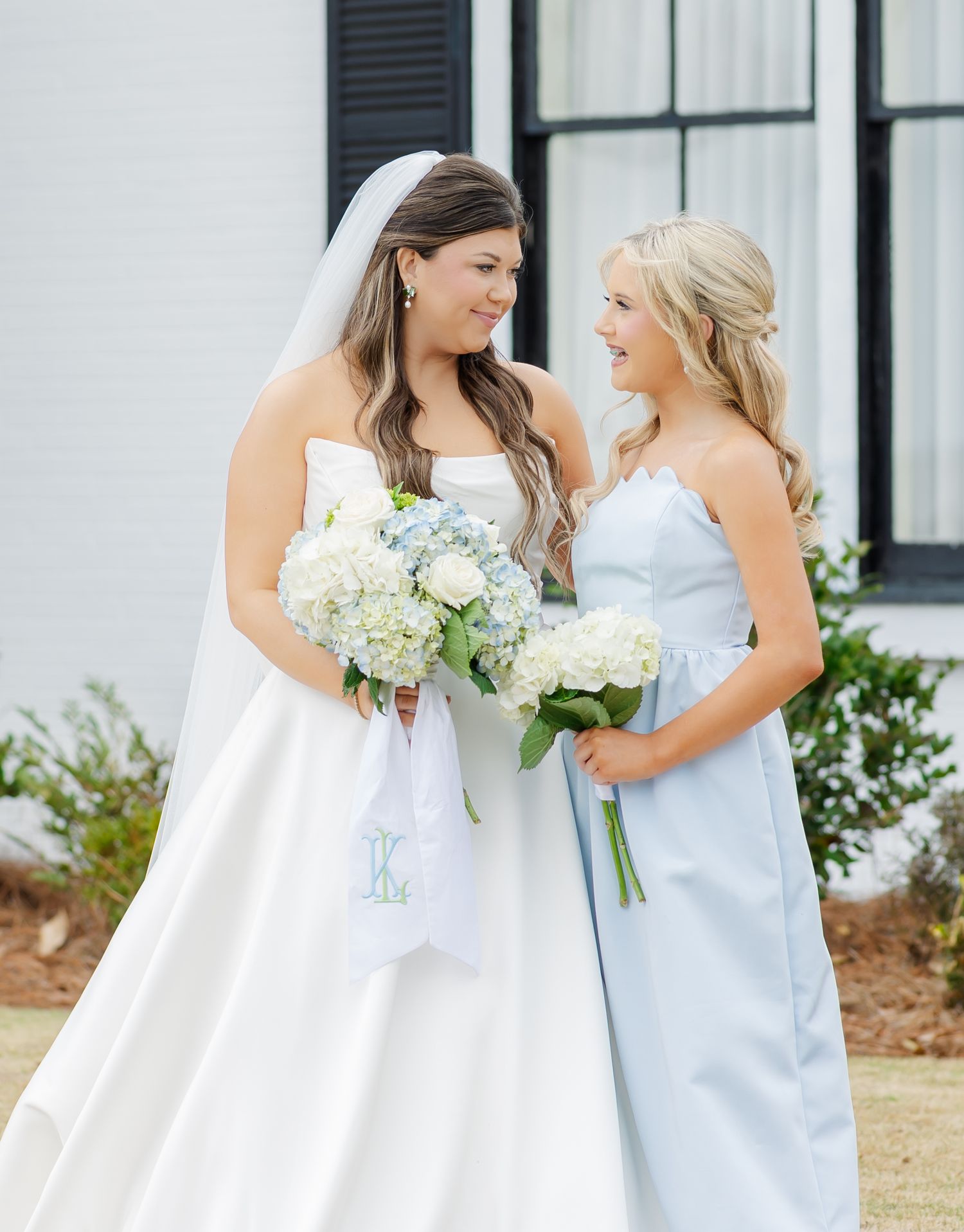 Bride in strapless white gown with veil and bridesmaid in light blue dress holding hydrangea bouquets.