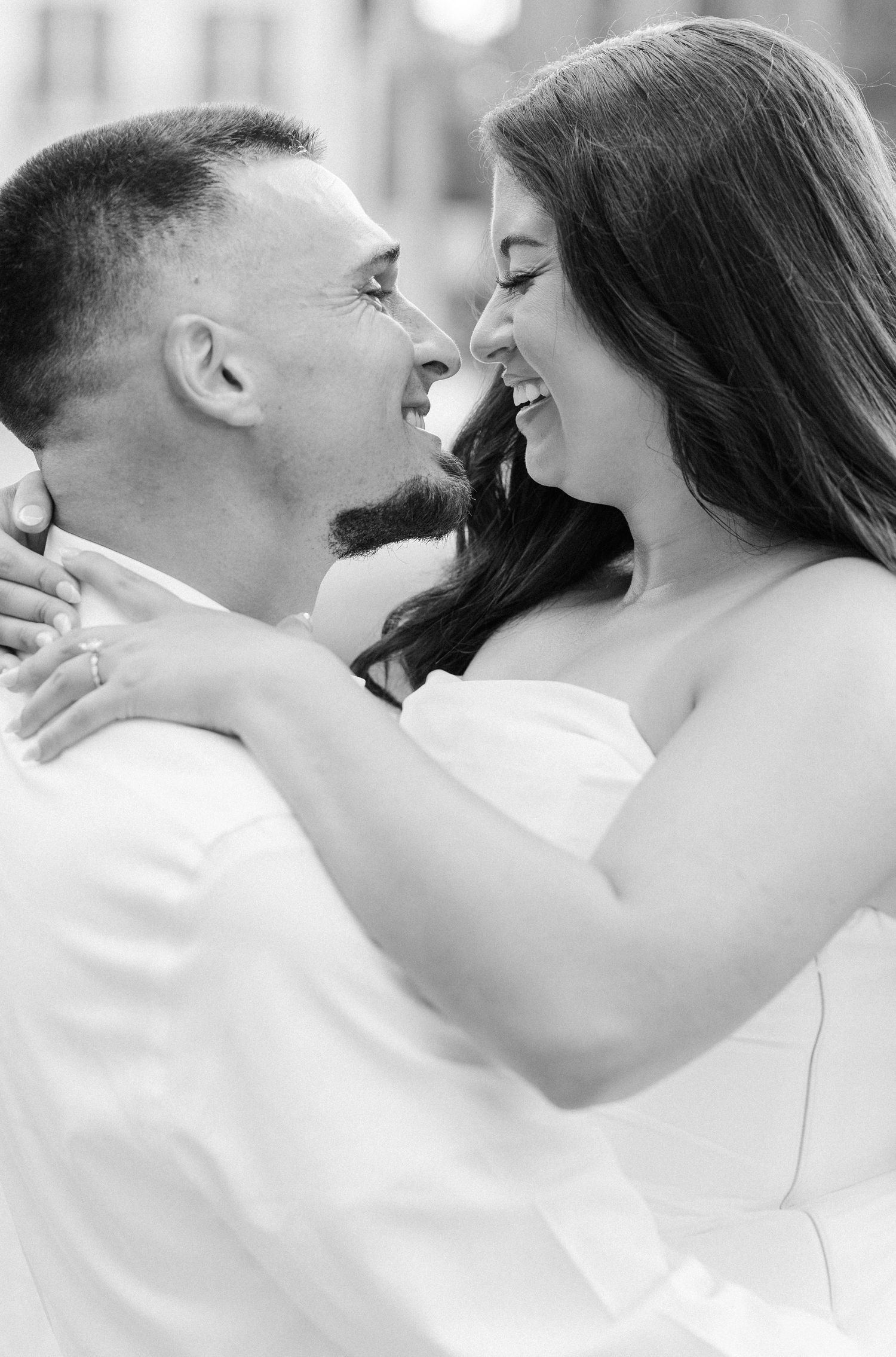 Black and white photo of a smiling couple in wedding attire sharing a romantic moment, the bride wearing a strapless gown.