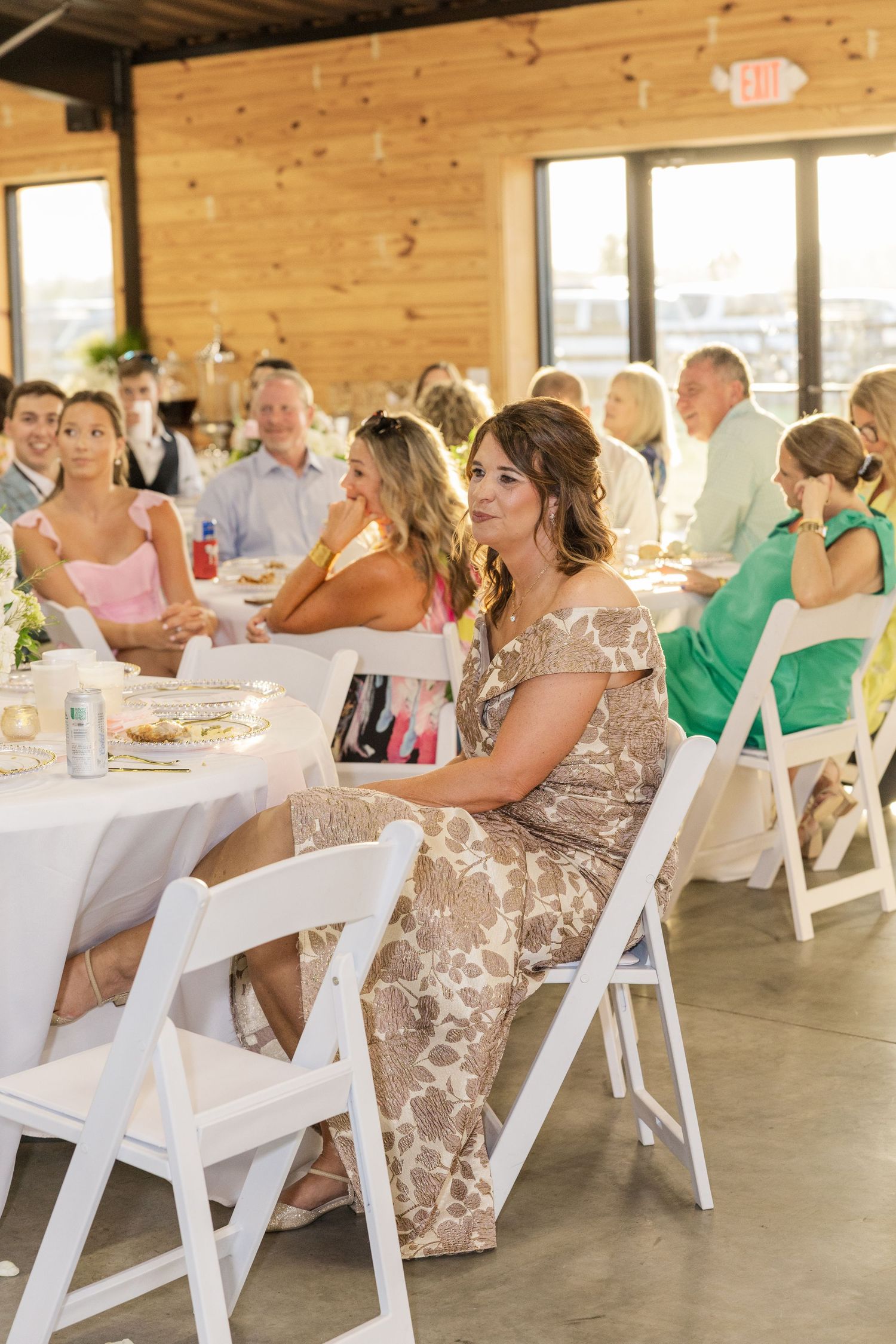 Wedding reception guests seated at white-clothed tables in a rustic wood-paneled venue.