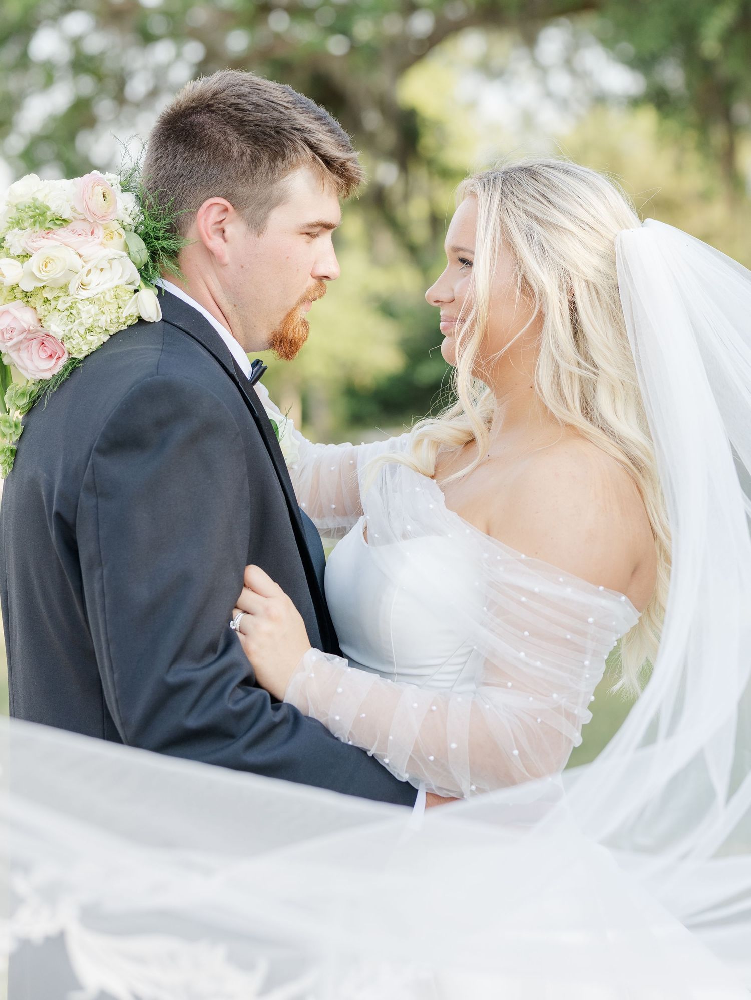 Romantic bride and groom portrait with flowing veil, bride in off-shoulder gown smiling at groom.