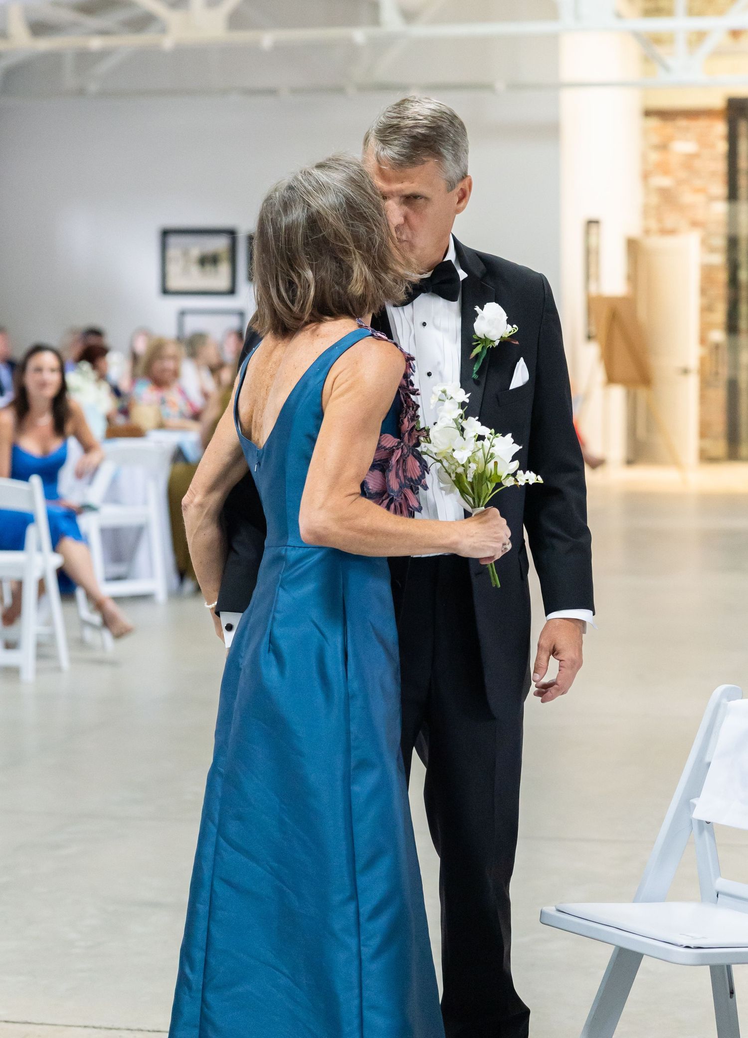 Couple sharing a tender kiss during wedding processional in bright modern ceremony venue.