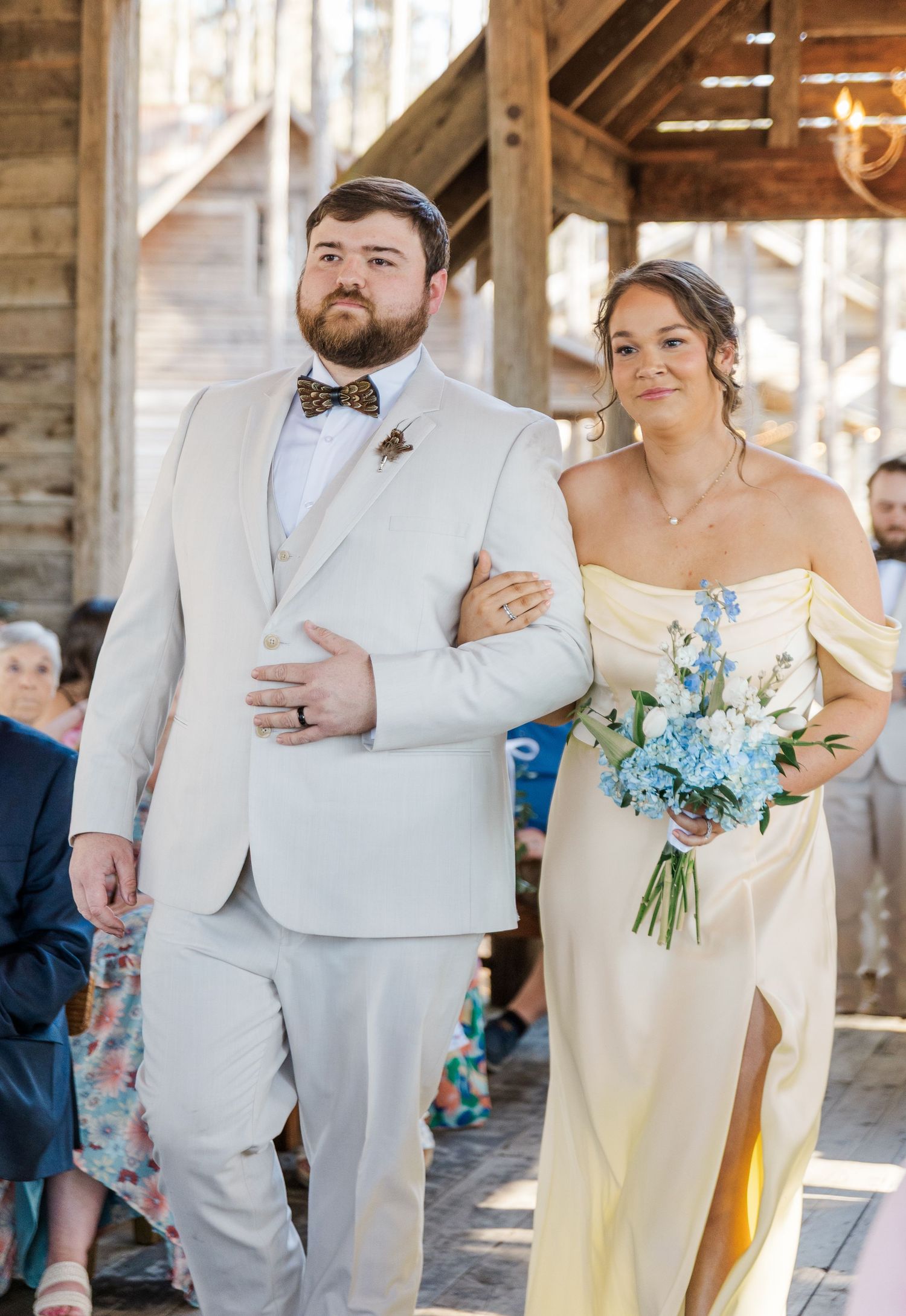 Bridesmaid in yellow gown walks down the aisle arm-in-arm with a groomsman in a beige suit.