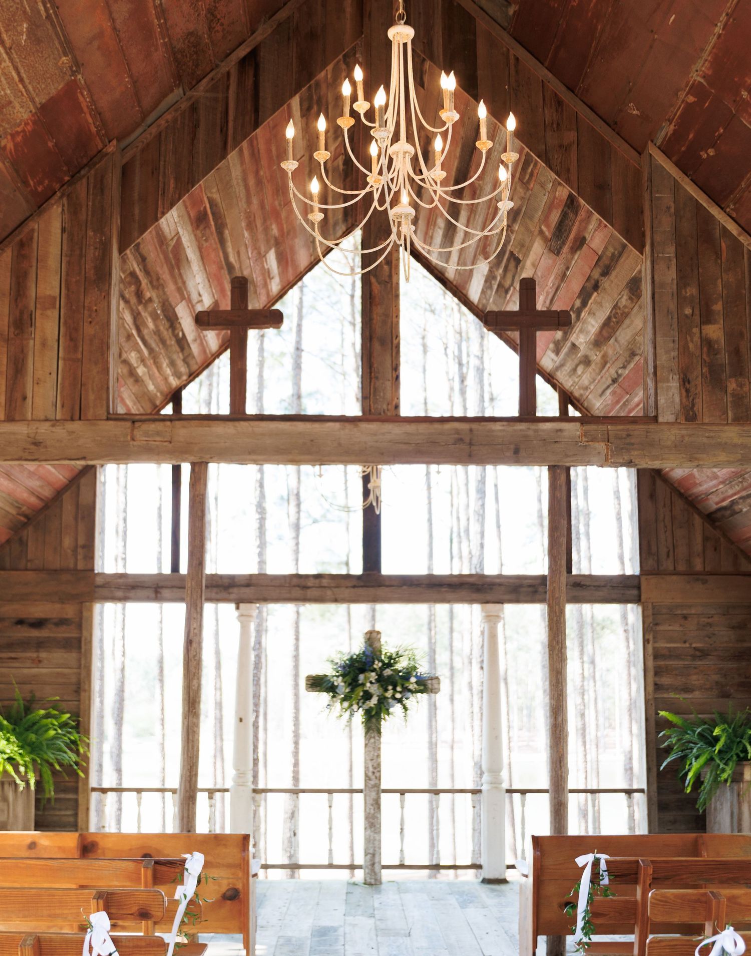 Rustic barn wedding chapel interior with wood walls, chandelier, crosses, and floral altar decor.
