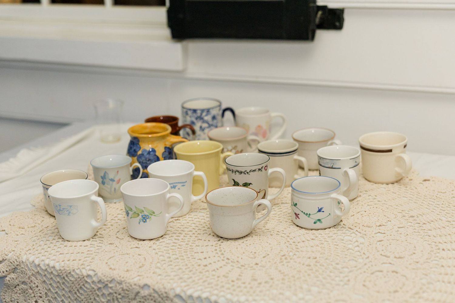 Collection of assorted ceramic coffee mugs displayed on a lace tablecloth.
