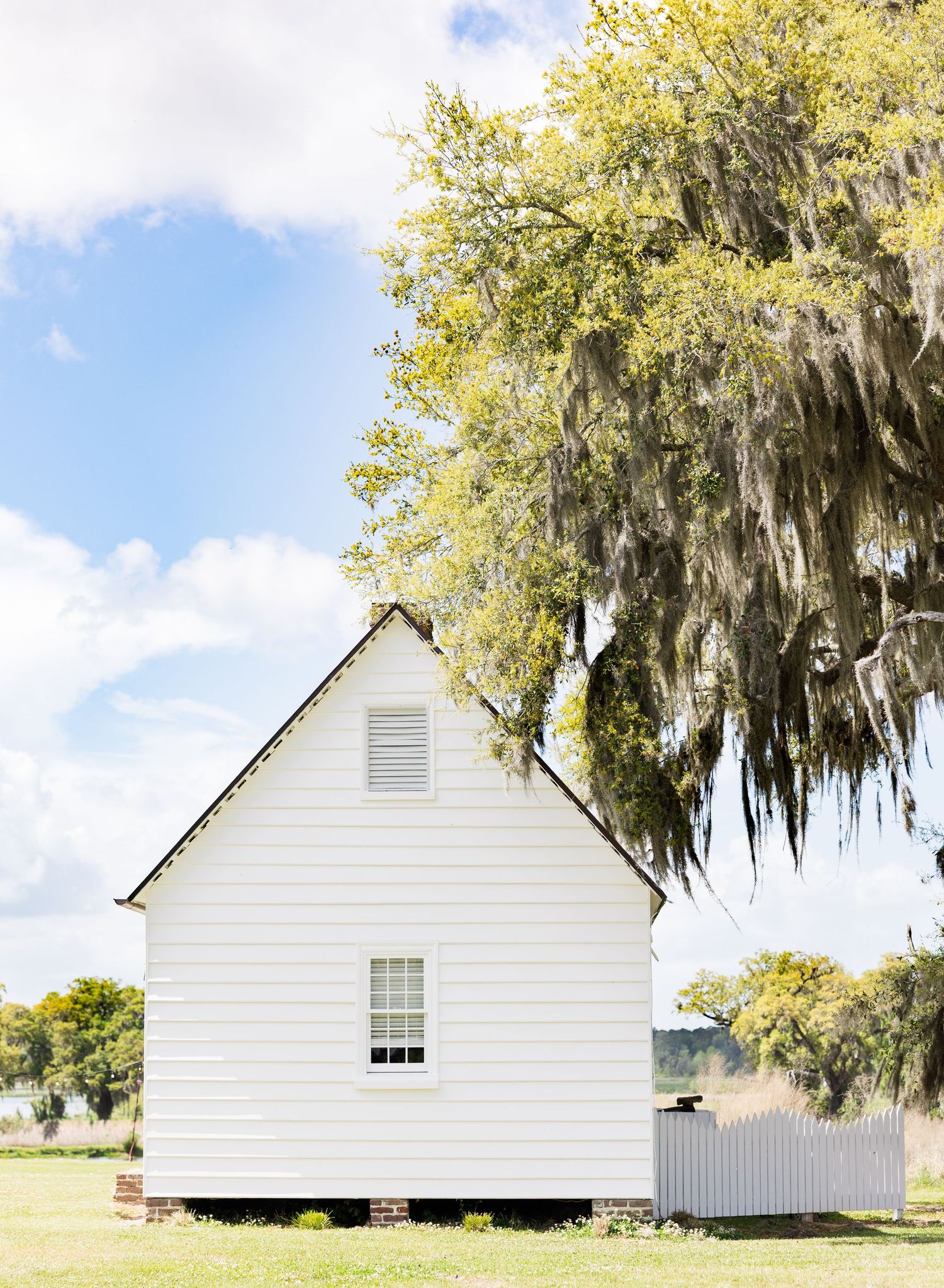 White clapboard chapel beside a moss-draped oak tree under blue sky.