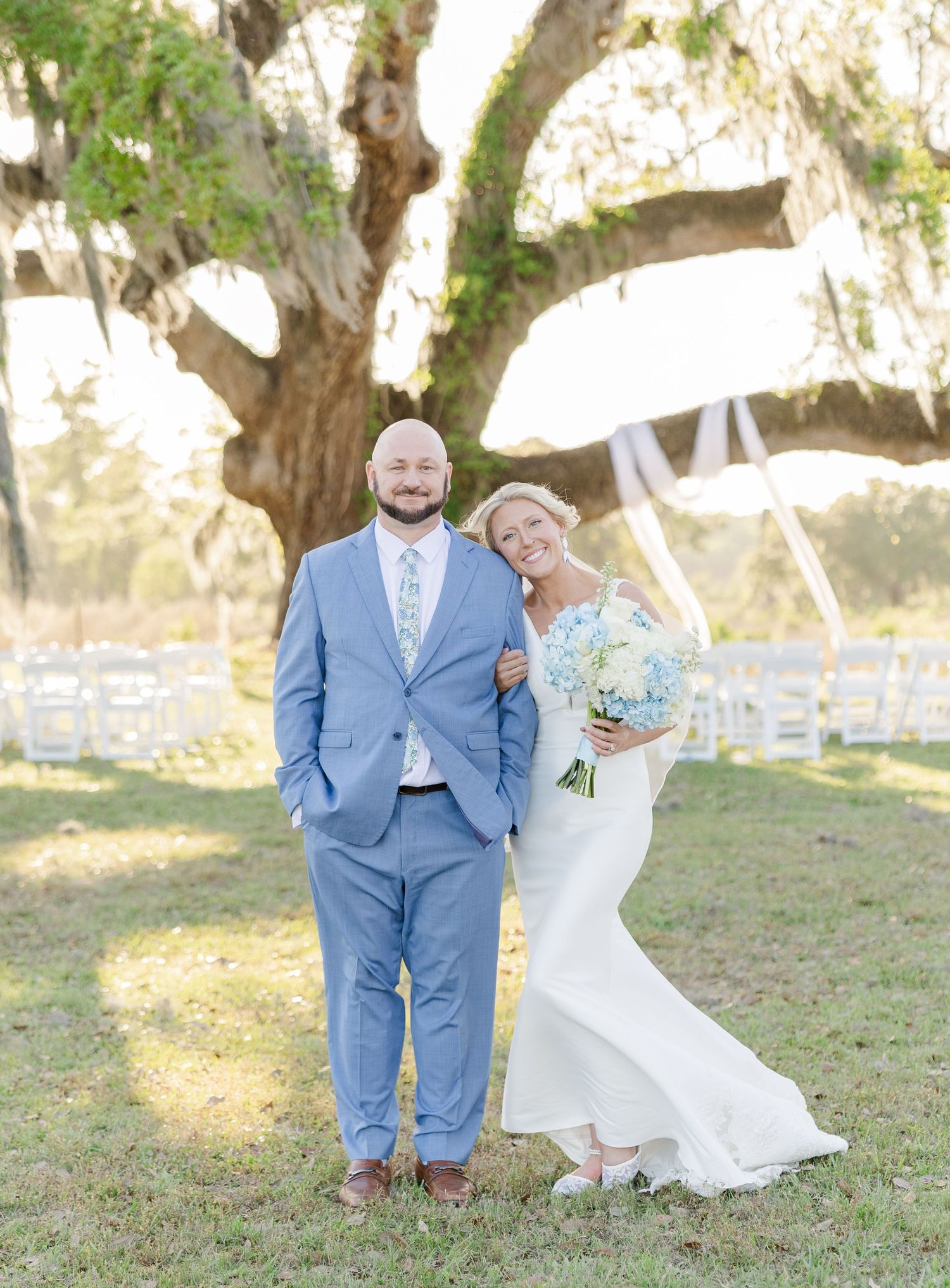 Bride and groom smiling together under a large oak tree at an outdoor wedding ceremony venue.