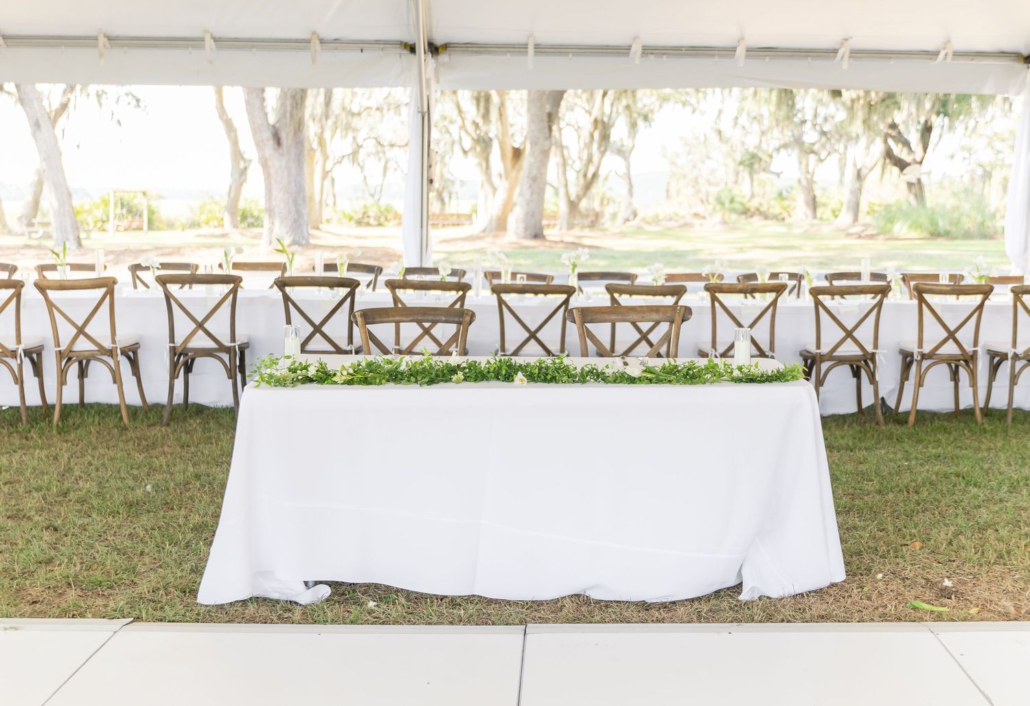 Long row of cross-back chairs and white-clothed tables set up for an outdoor wedding reception.