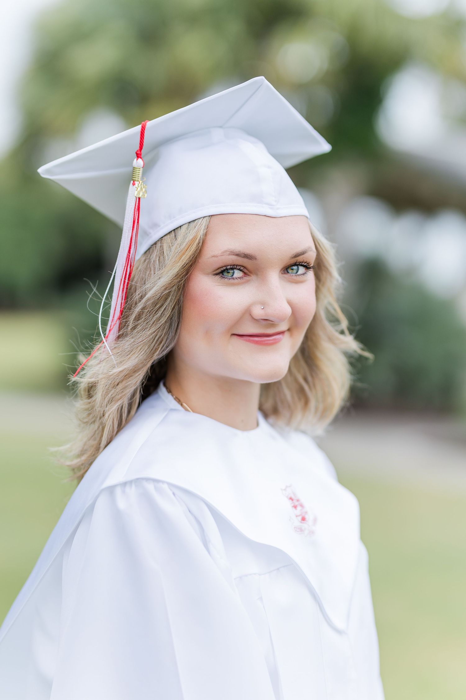Graduate wearing white cap and gown poses outdoors during a graduation photoshoot.