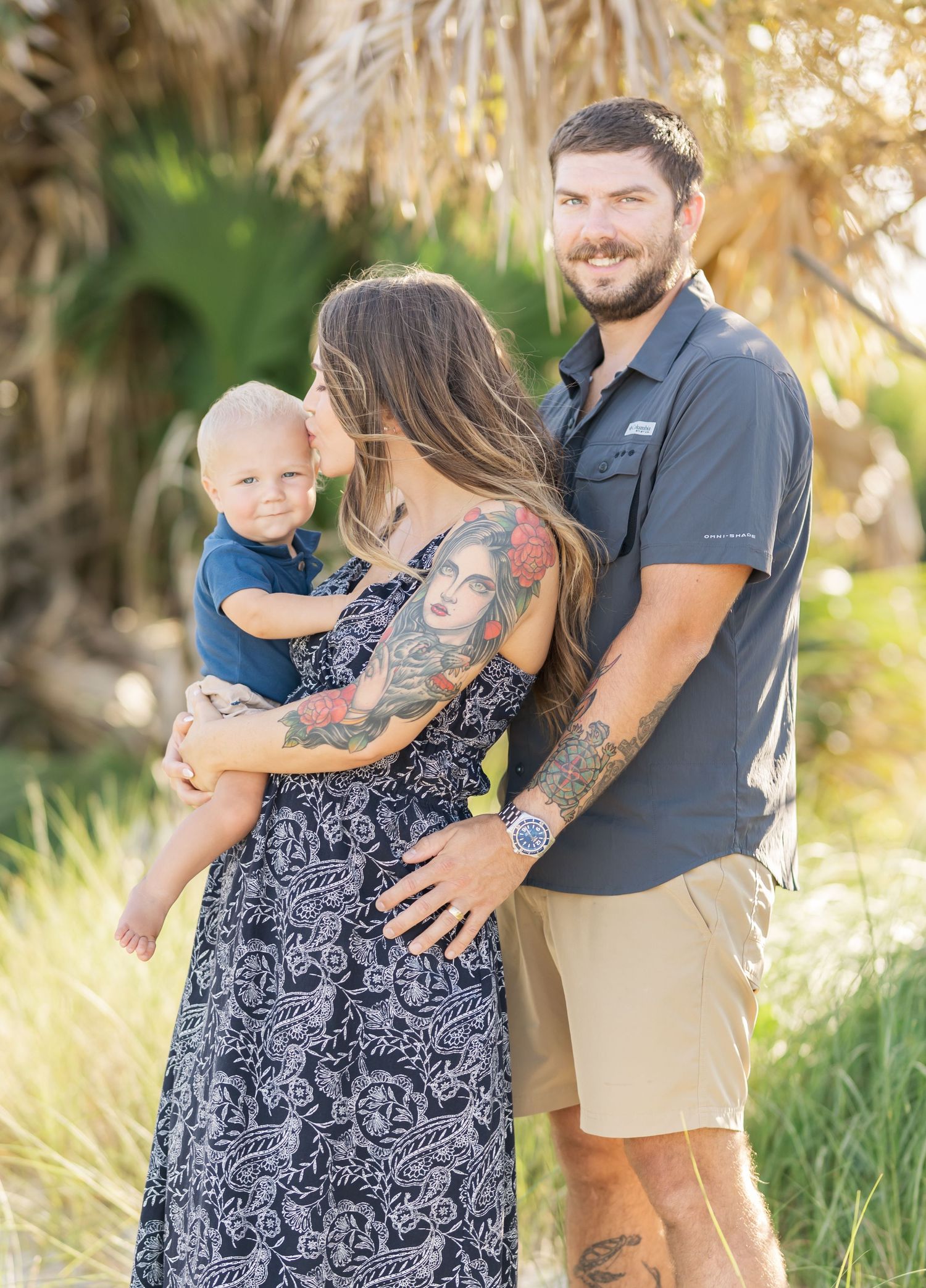 A family in casual attire poses together outdoors among palm trees during golden hour lighting.
