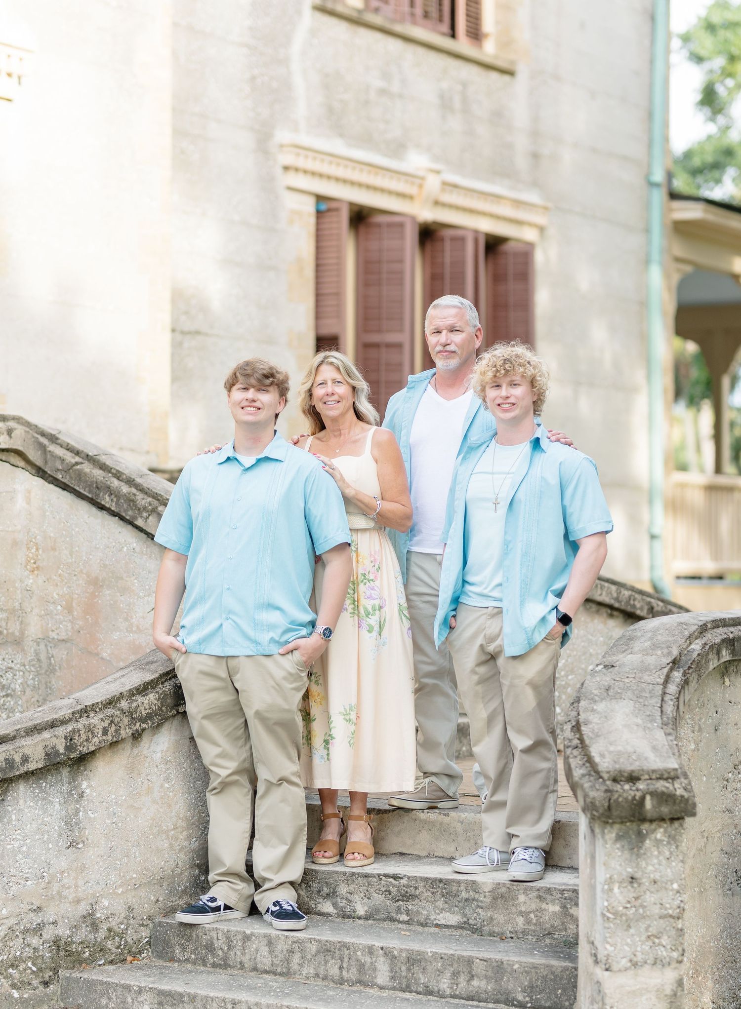 Family poses together on stone steps of historic building wearing coordinated light blue and khaki outfits.