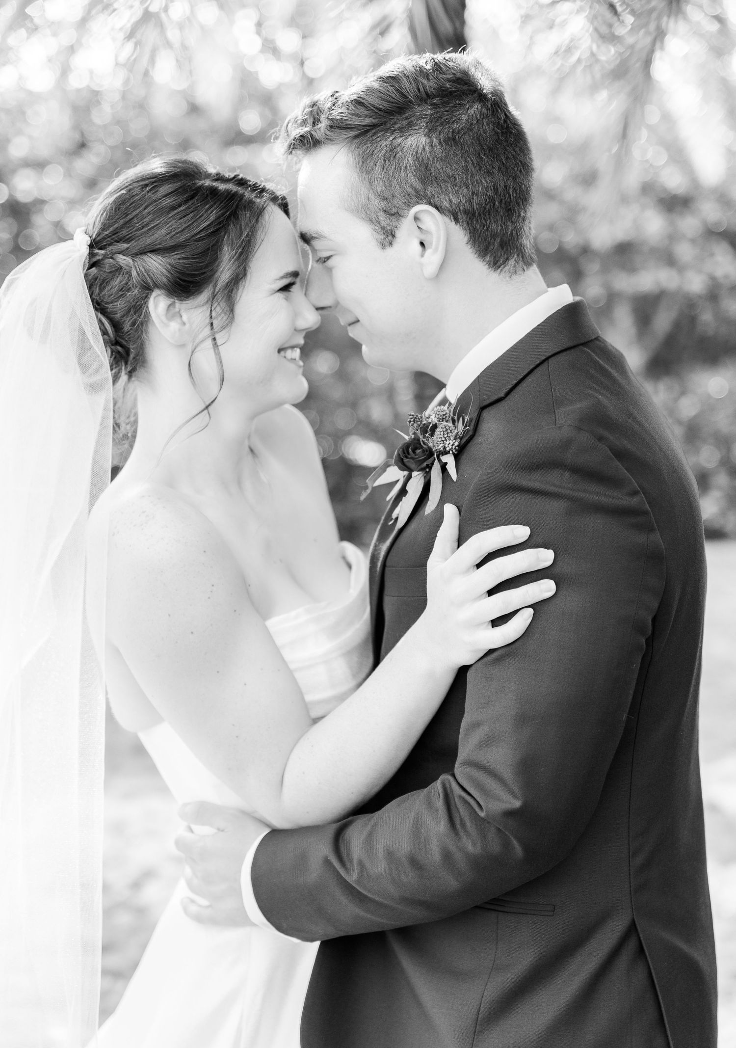 Black and white intimate portrait of newlyweds sharing a tender moment outdoors.