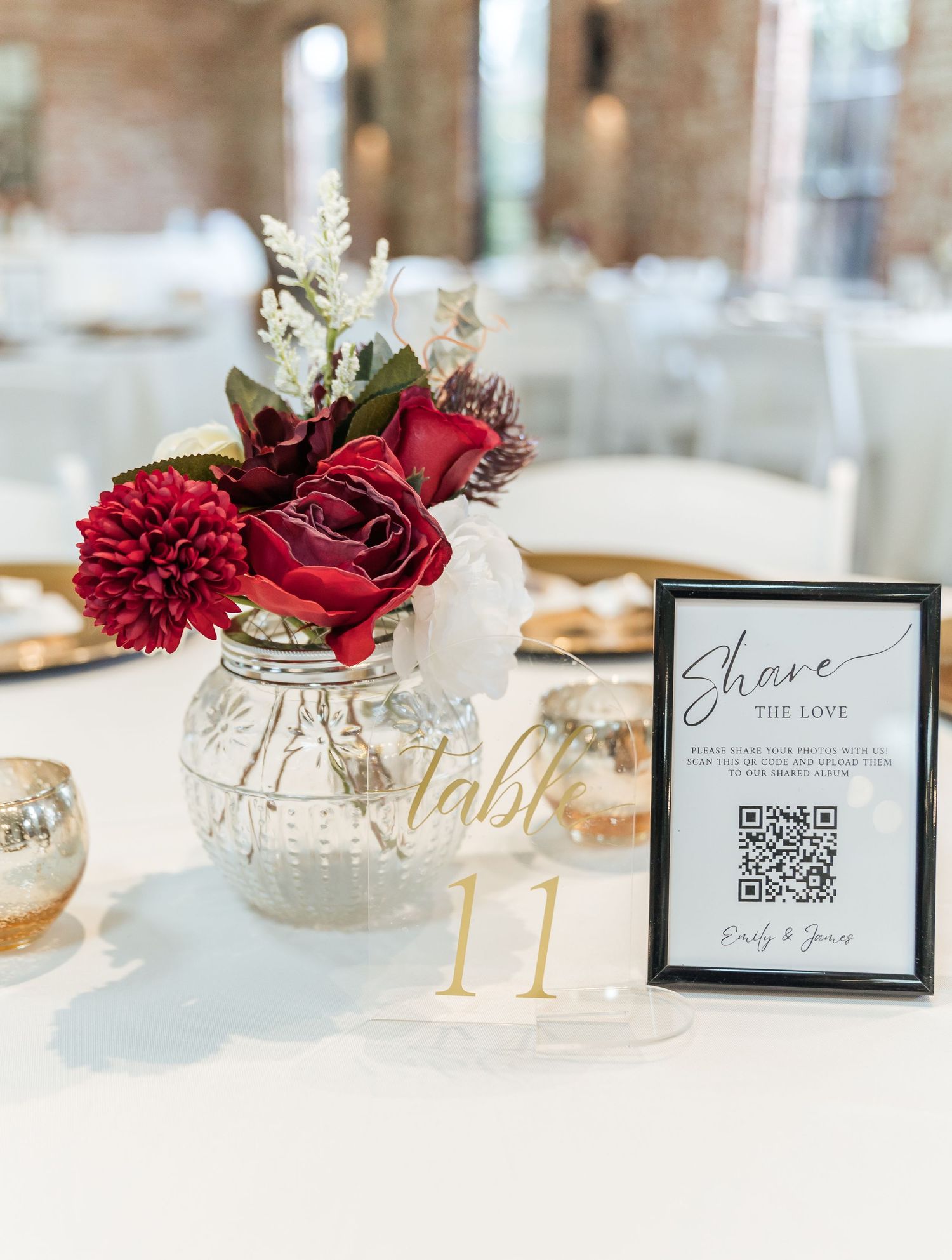 Wedding table centerpiece with red roses and white flowers in mason jar next to QR code sign and table number.